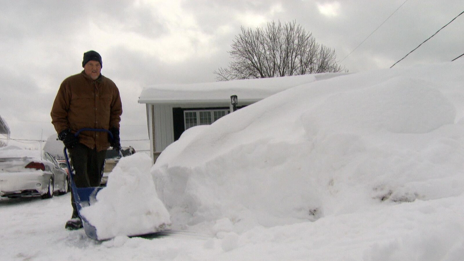Luc Cayer pousse la neige de son entrée vers l'intérieur de son terrain avec une grosse pelle bleue.