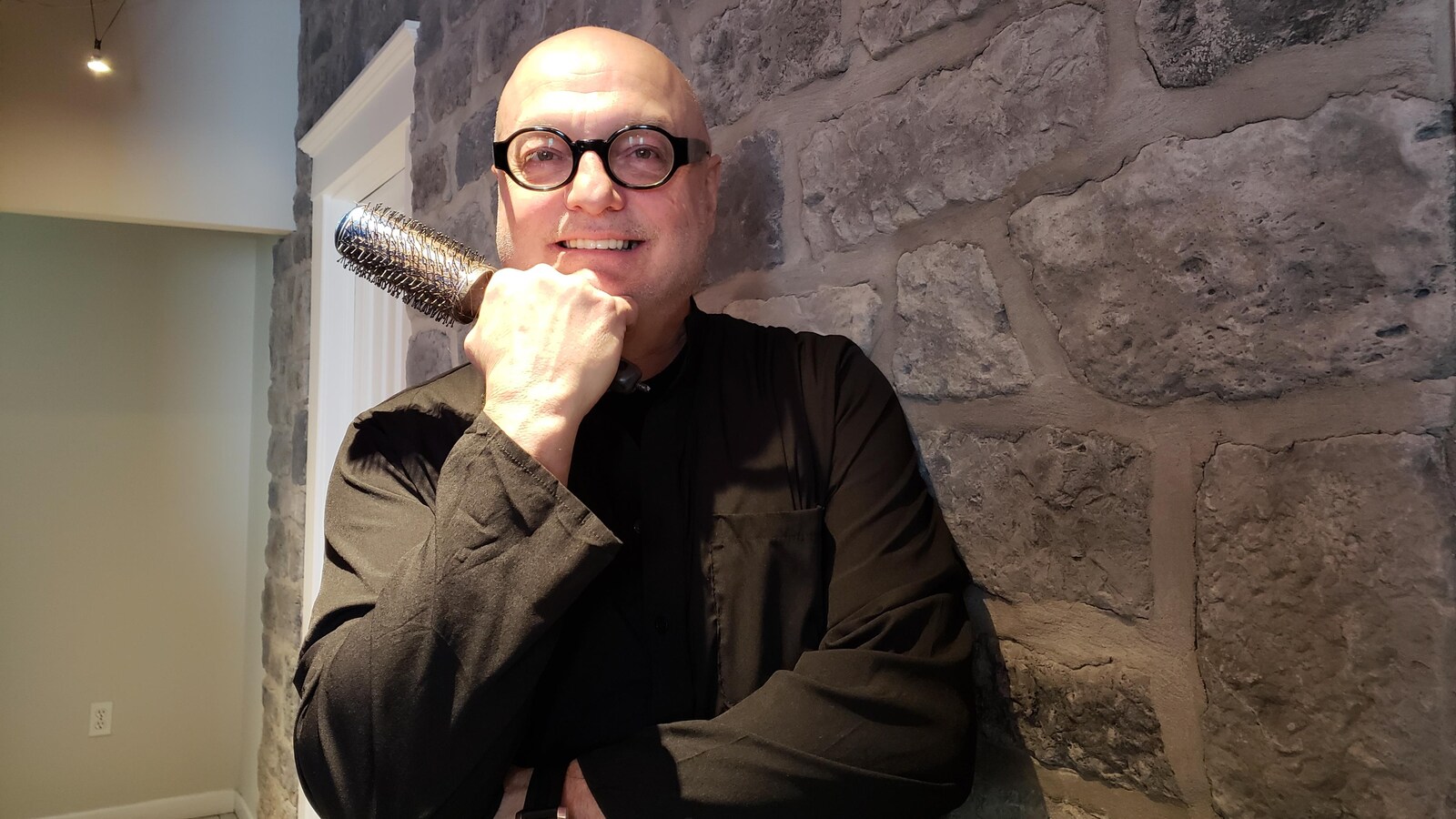 Luc Lussier devant un mur de pierre avec une brosse dans les mains.
