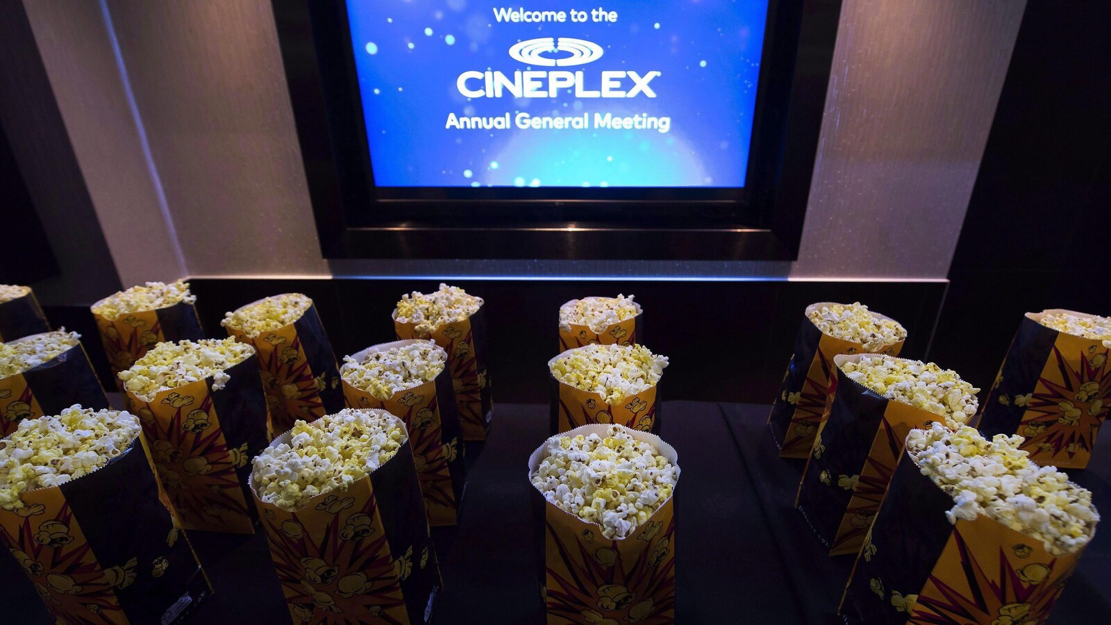 Des sacs remplis de maïs soufflé sont disposés devant un écran qui affiche le logo de Cineplex.