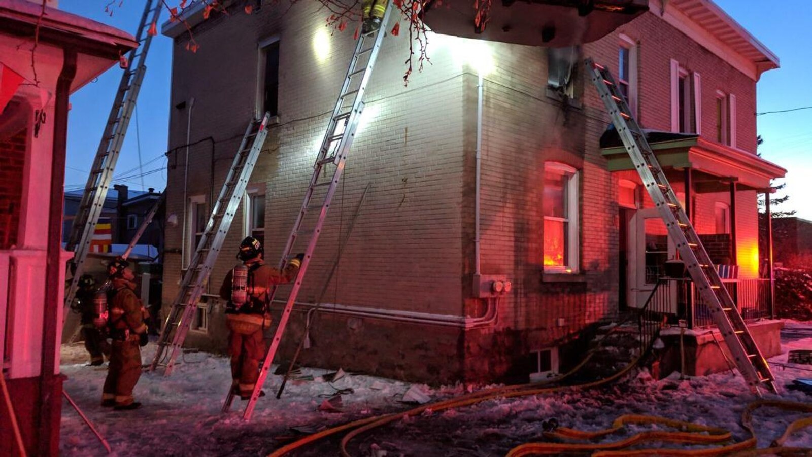 Des pompiers au pied d'échelles près d'une maison en hiver pendant la soirée.