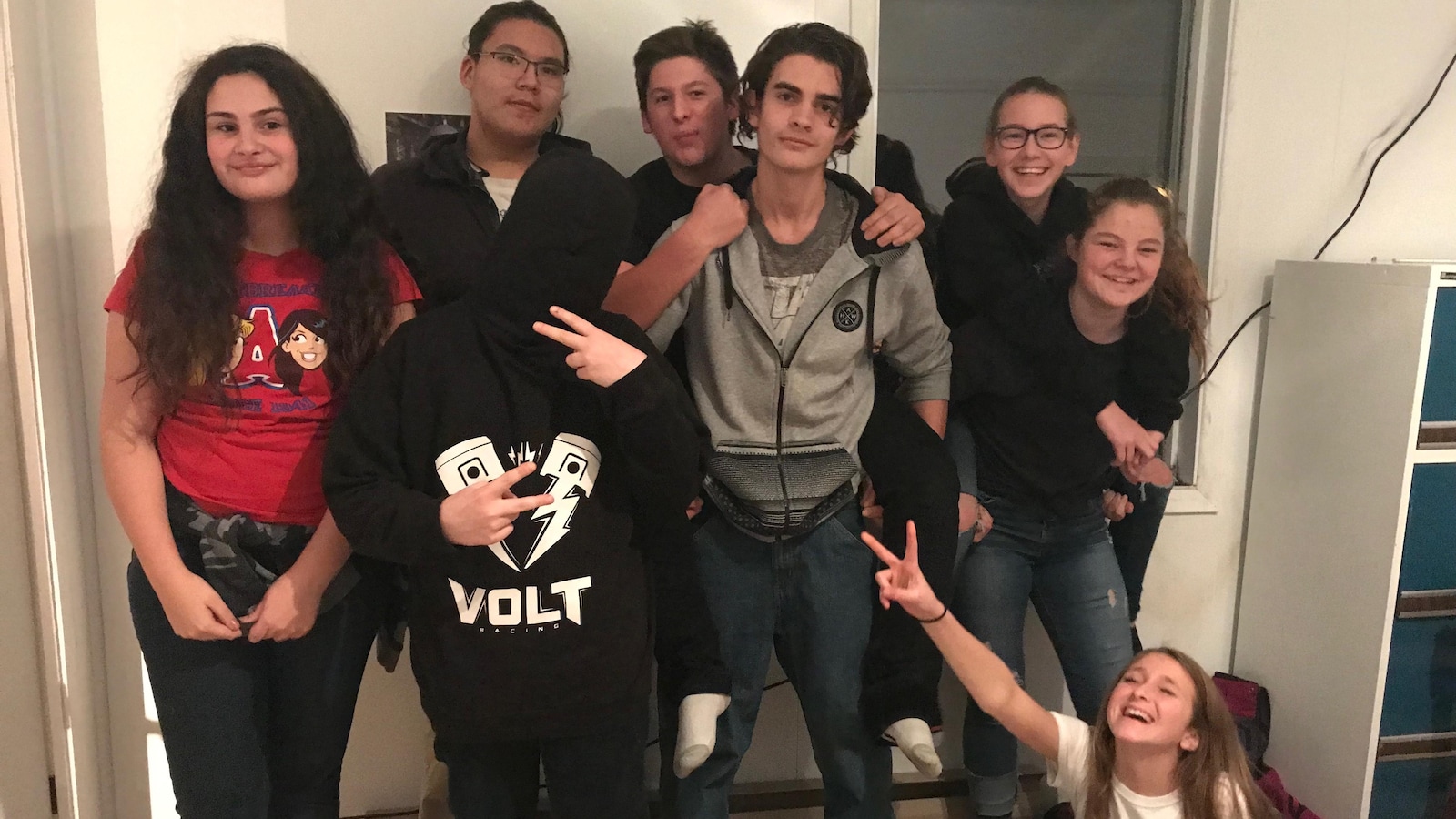 Des adolescents posent pour la caméra, certains riant, d'autres faisant des signes de paix.
