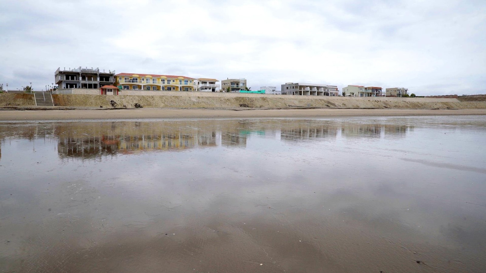Des maisons alignées sur le front de mer. Elles se reflètent sur le sable humide.