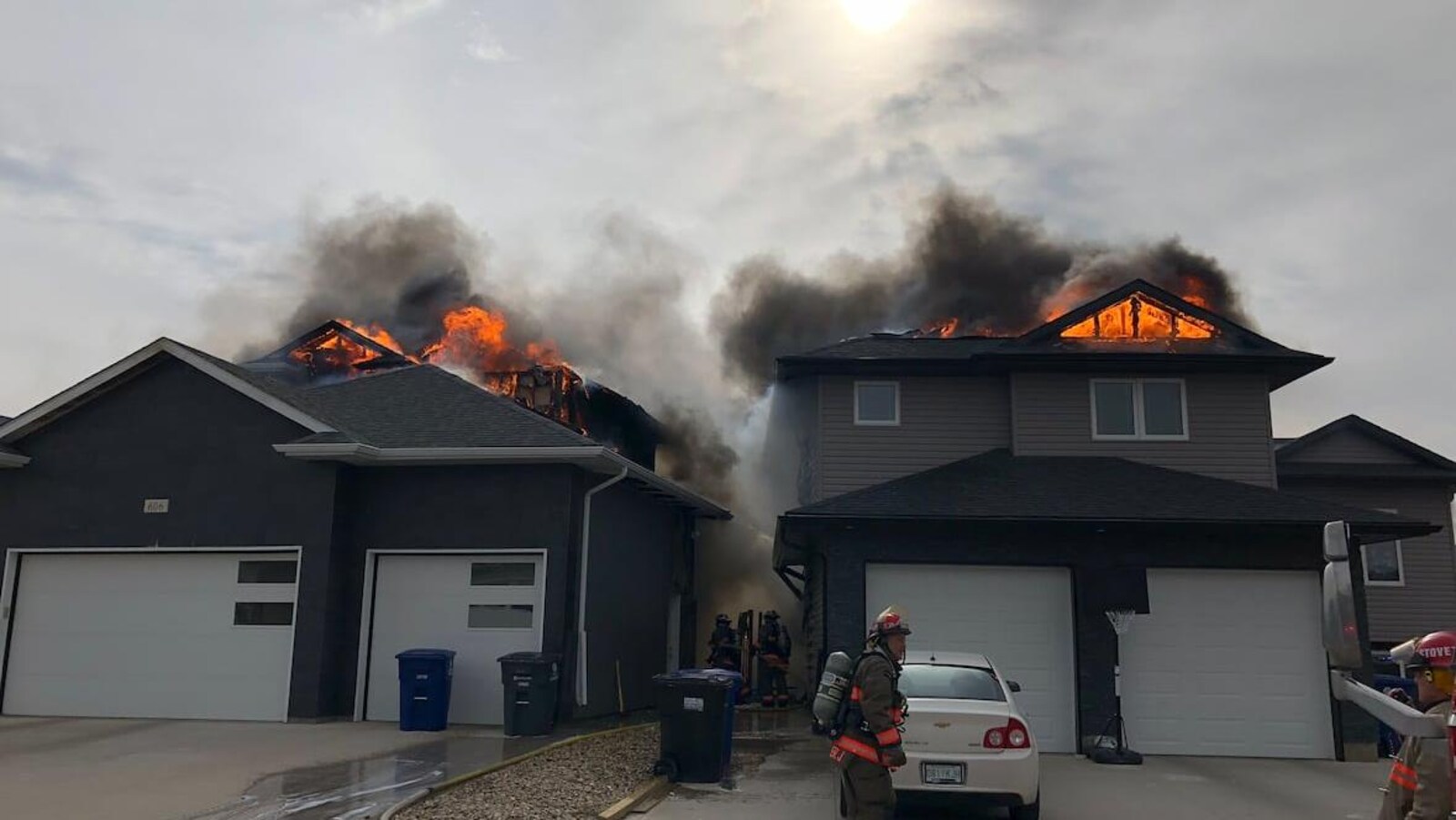Des pompiers se tiennent près des deux maisons en feu.