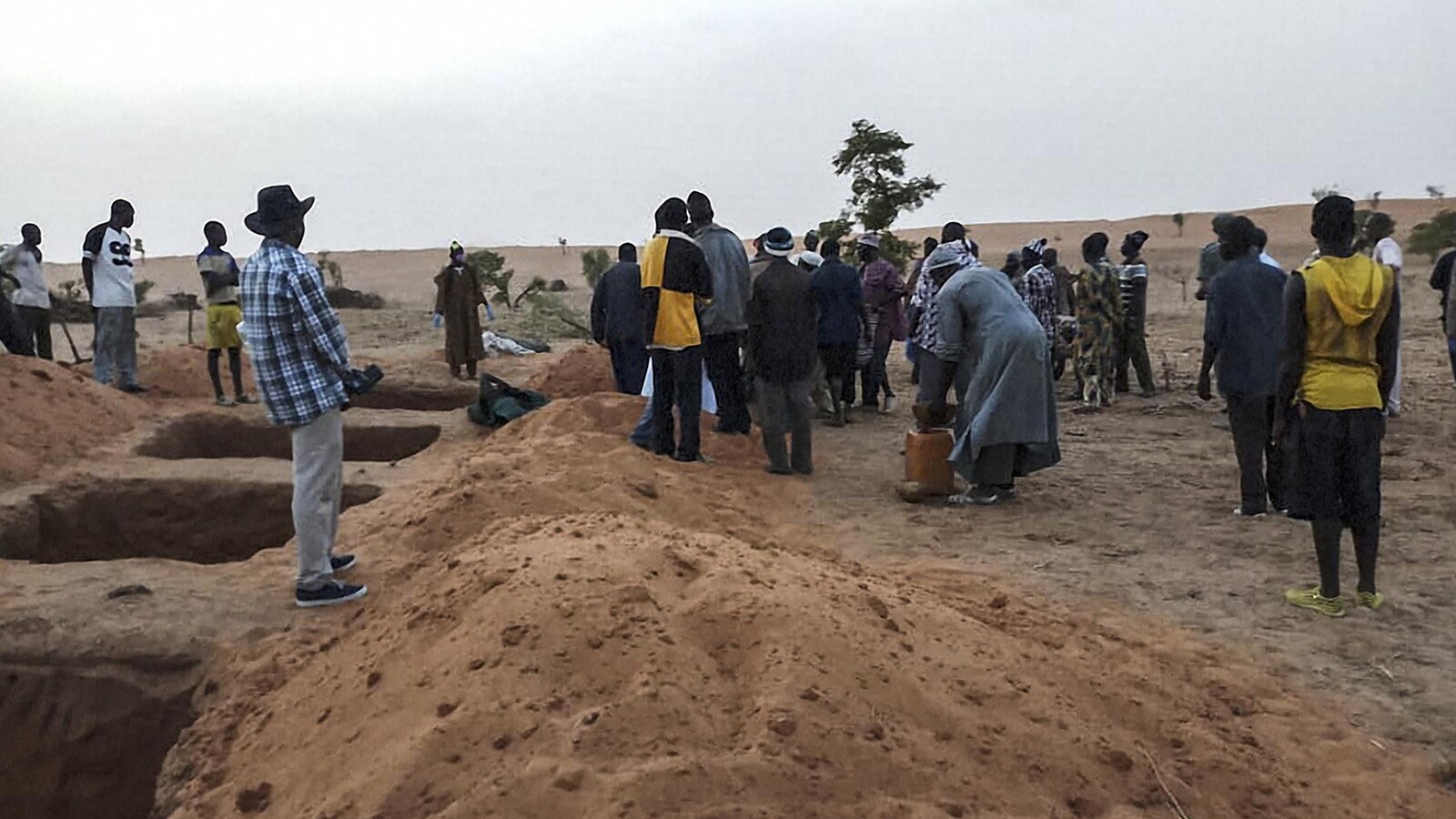 Plusieurs Maliens sont debout près de fosses creusées dans le sable.