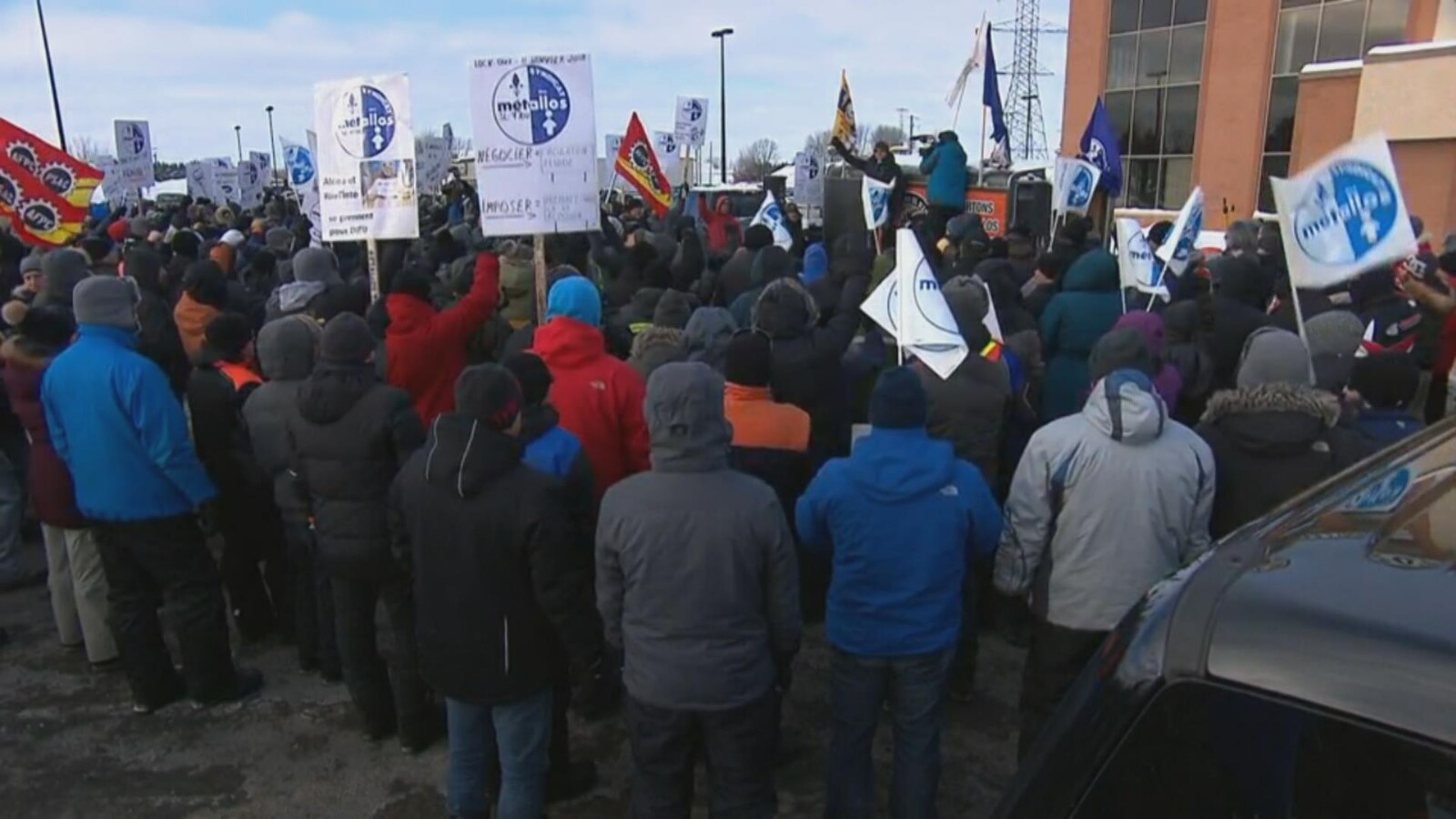 Des manifestants tiennent des pancartes alors qu'un homme s'adresse à eux en levant le poing.