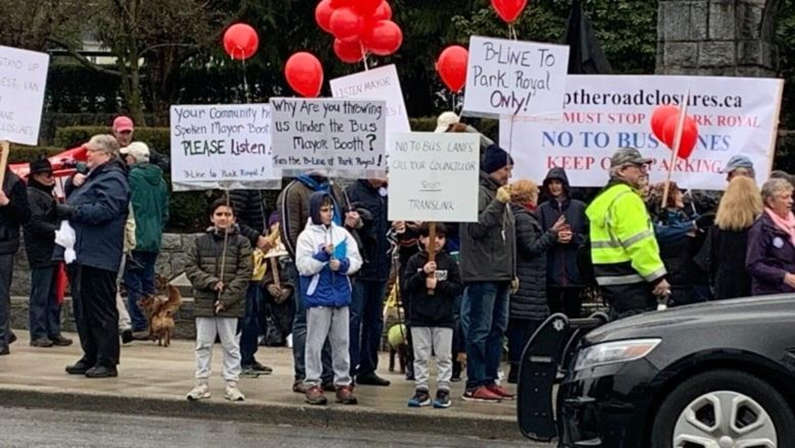 Des dizaines de manifestants brandissant des pancartes et tenant à la main des ballons rouges dénoncent un nouveau couloir d'autobus à West Vancouver.