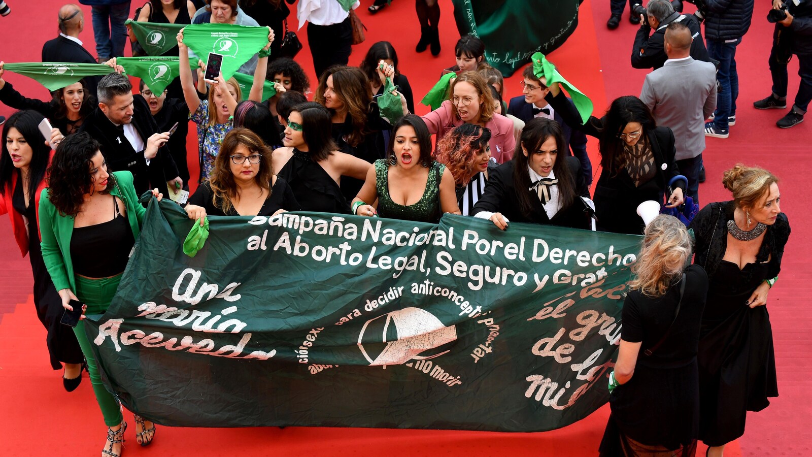 Des militantes tiennent une banderole et brandissent des foulards sur le tapis rouge à Cannes.