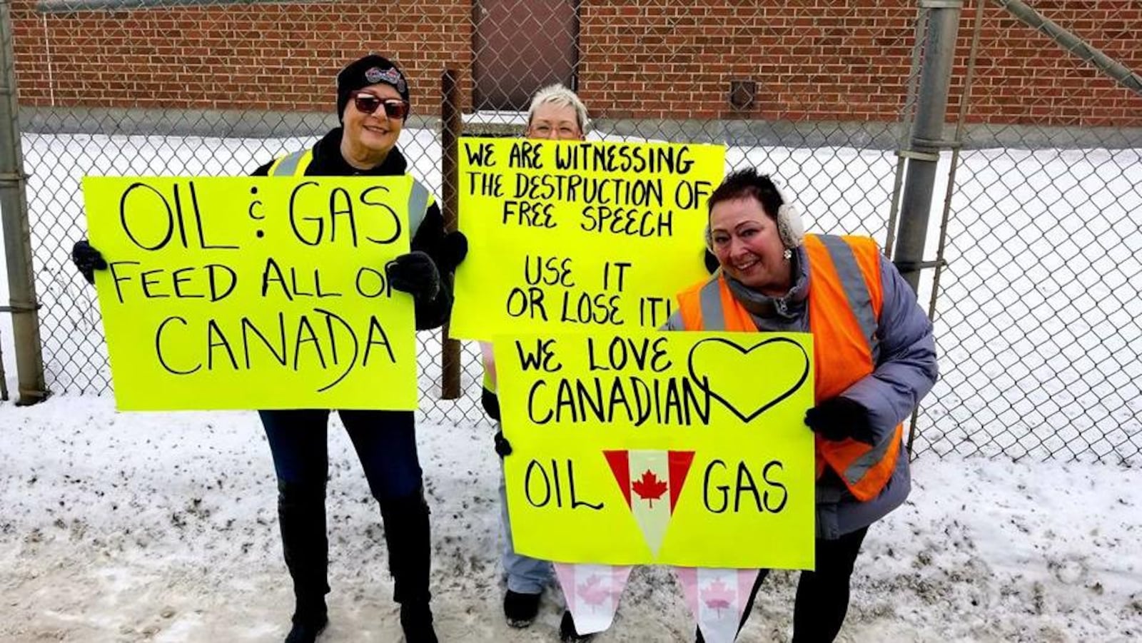 Trois manifestantes à Brandon debout sur la neige brandissent des pancartes qui appuient l'industrie pétrolière et gazière.