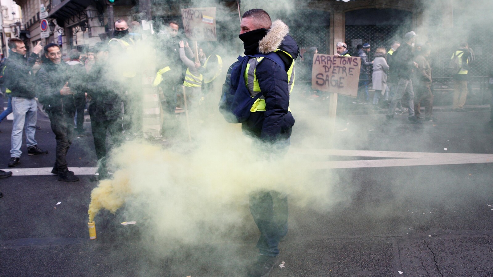 Un manifestant en gilet jaune dans une nuage de fumigène.