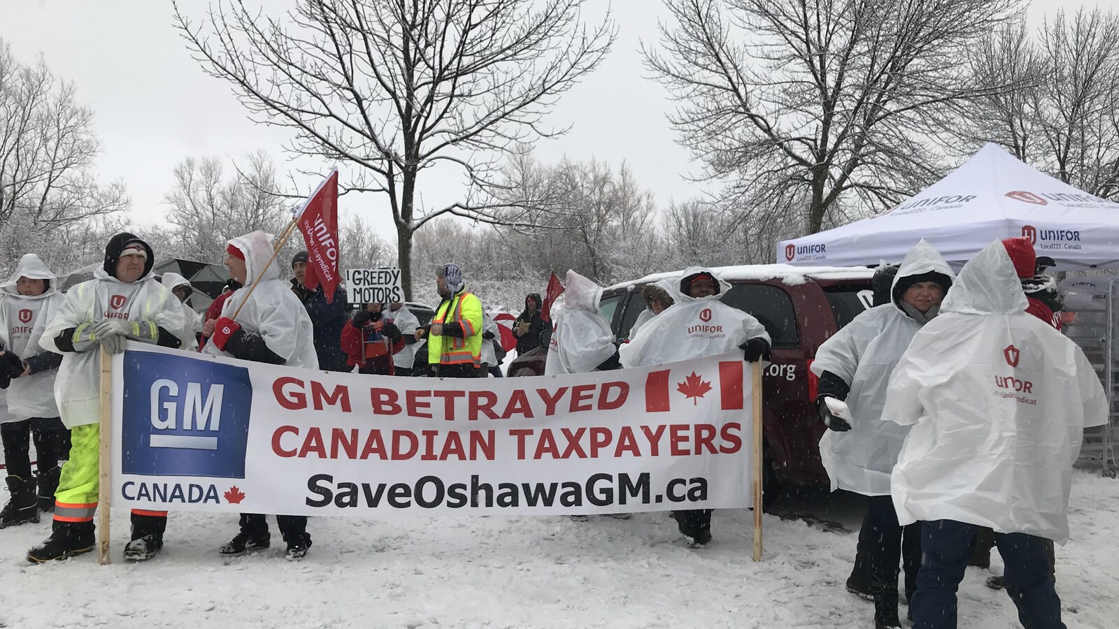 Photo d'hommes à l'extérieur dans la neige tenant une banderole où on peut lire : « GM a trahi les contribuables canadiens ».