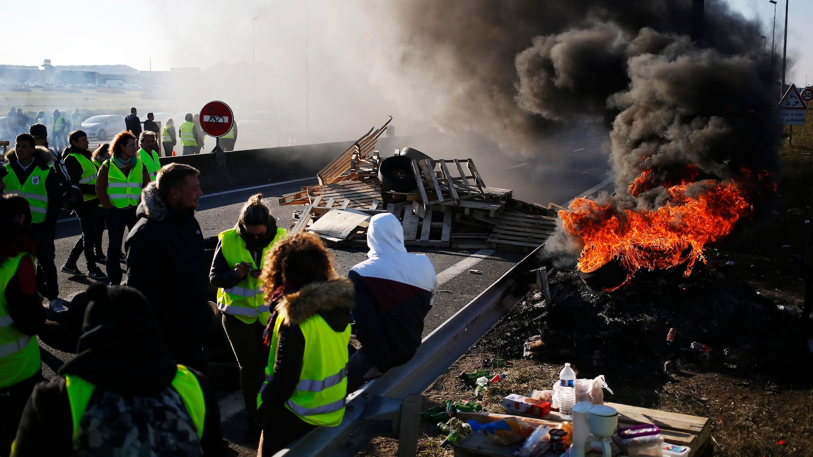 Un blocage routier avec un incendie et des citoyens arborant un gilet jaune.