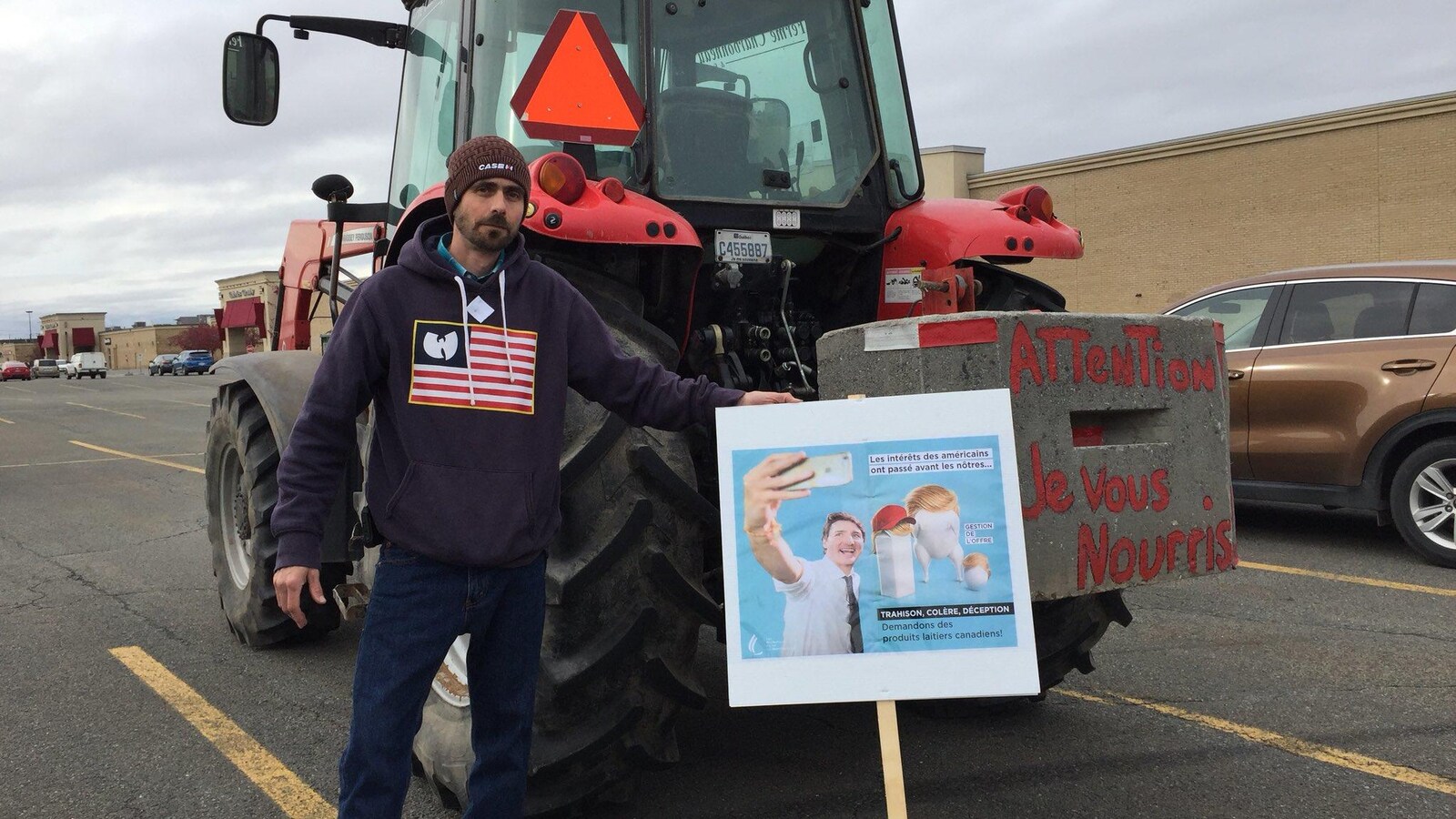 Un producteur de lait devant son tracteur avec une pancarte où on voit Justin Trudeau.