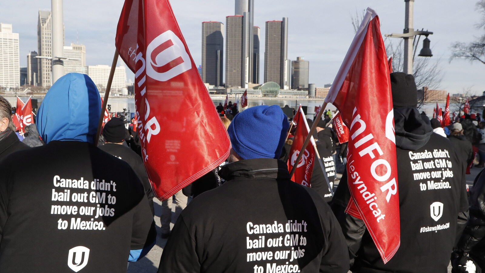 Des syndiqués portent des drapeaux d'Unifor et des vestes sur lesquelles il est écrit en anglais : « Le Canada n'a pas renfloué GM pour déménager nos emplois au Mexique ».