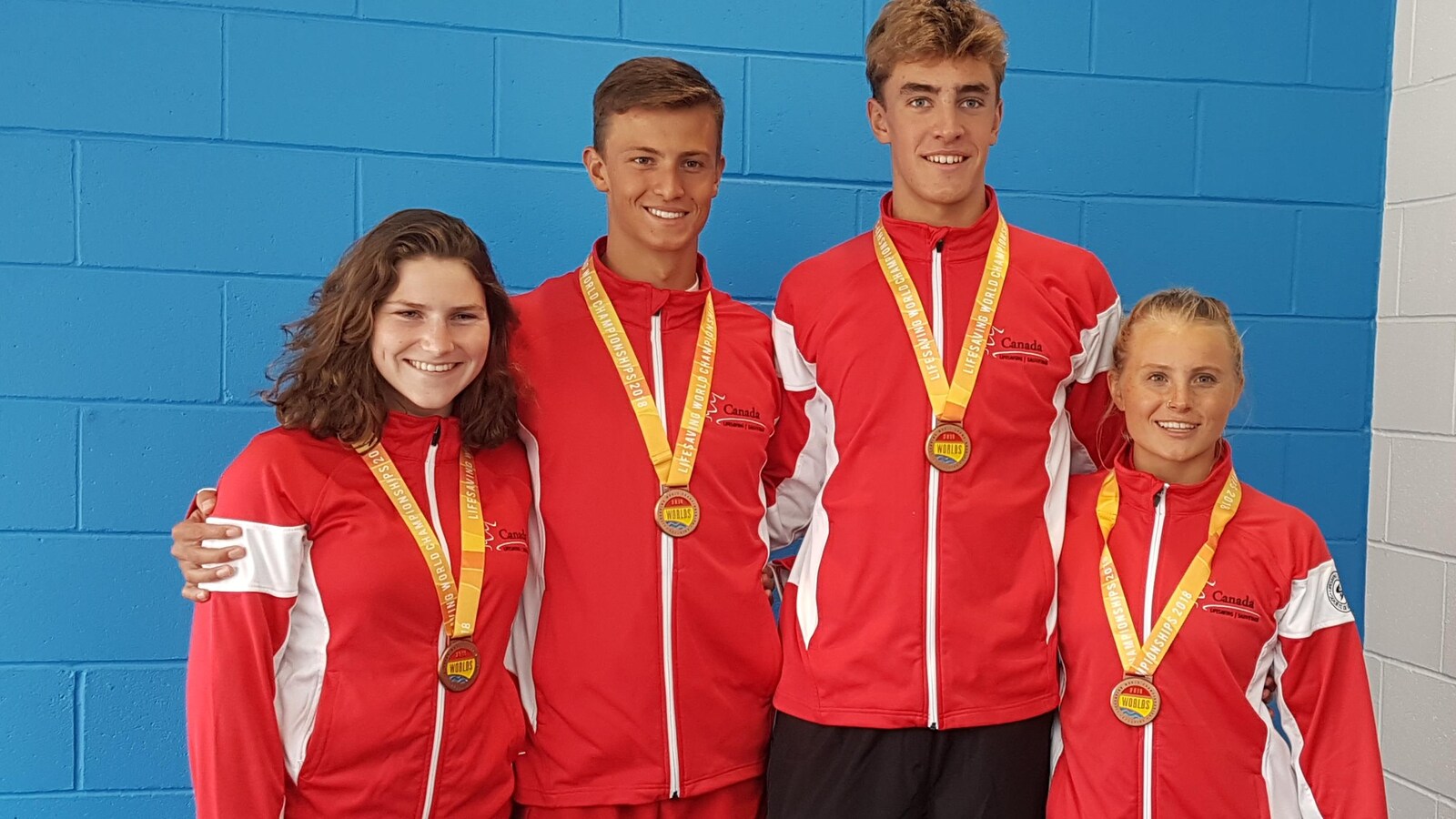 Quatre jeunes athlètes posent avec leur médaille, sur un podium.