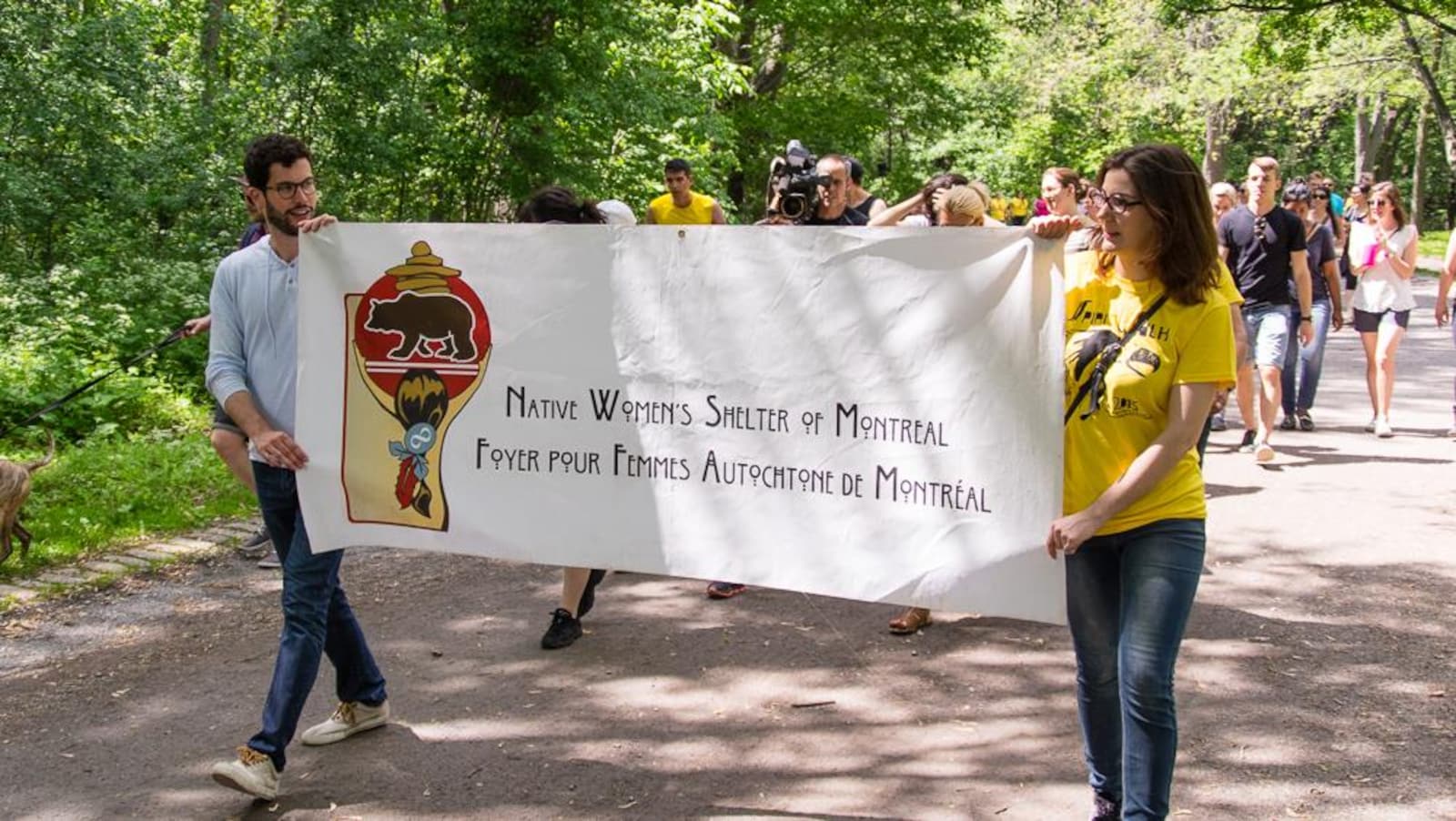Deux personnes tiennent une bannière avec les mots «Foyer pour femmes autochtones de Montréal» dessus. D'autres personnes les suivent à la marche derrière.