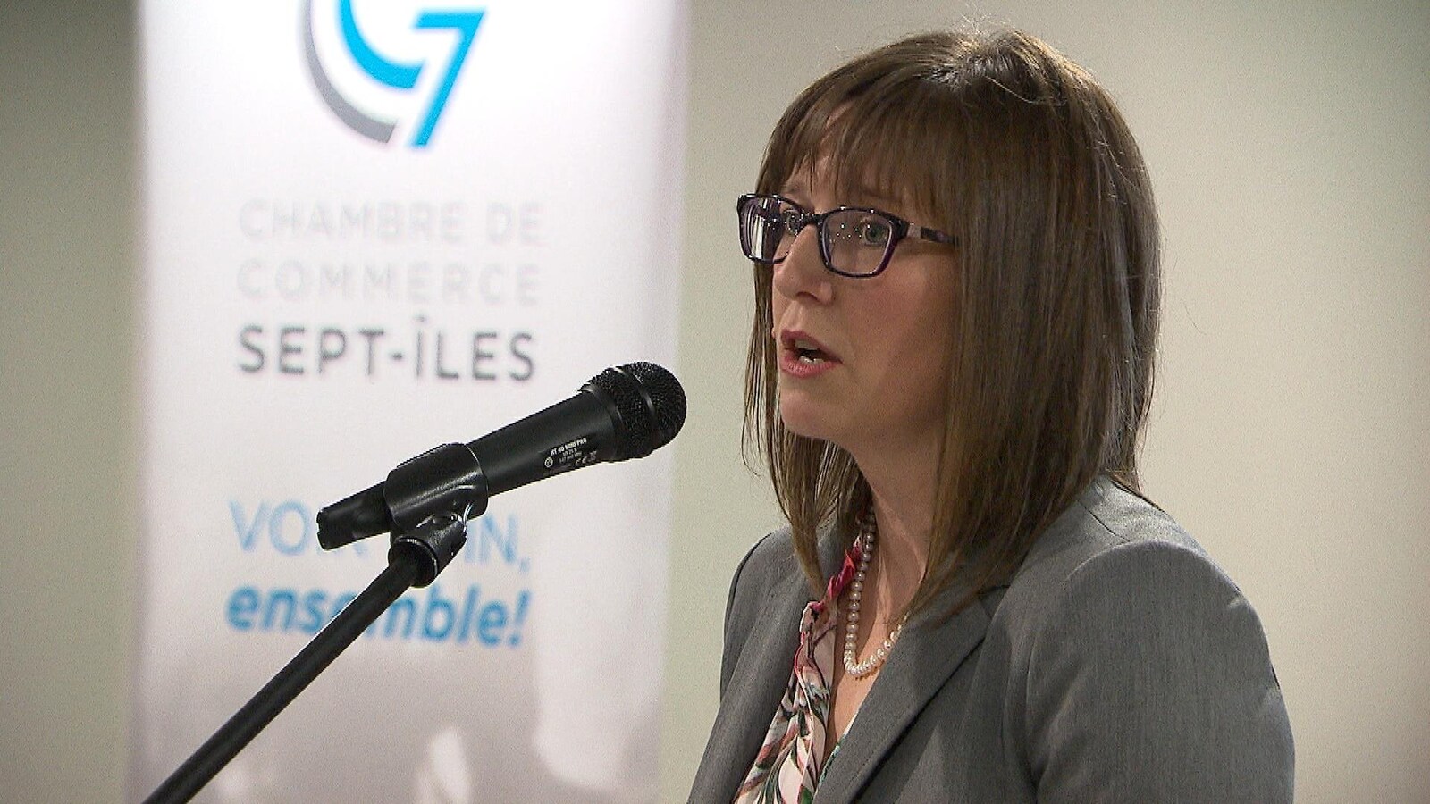 Elle est au micro avec à côté d'elle une banderole avec le logo de la Chambre de commerce de Sept-Îles.