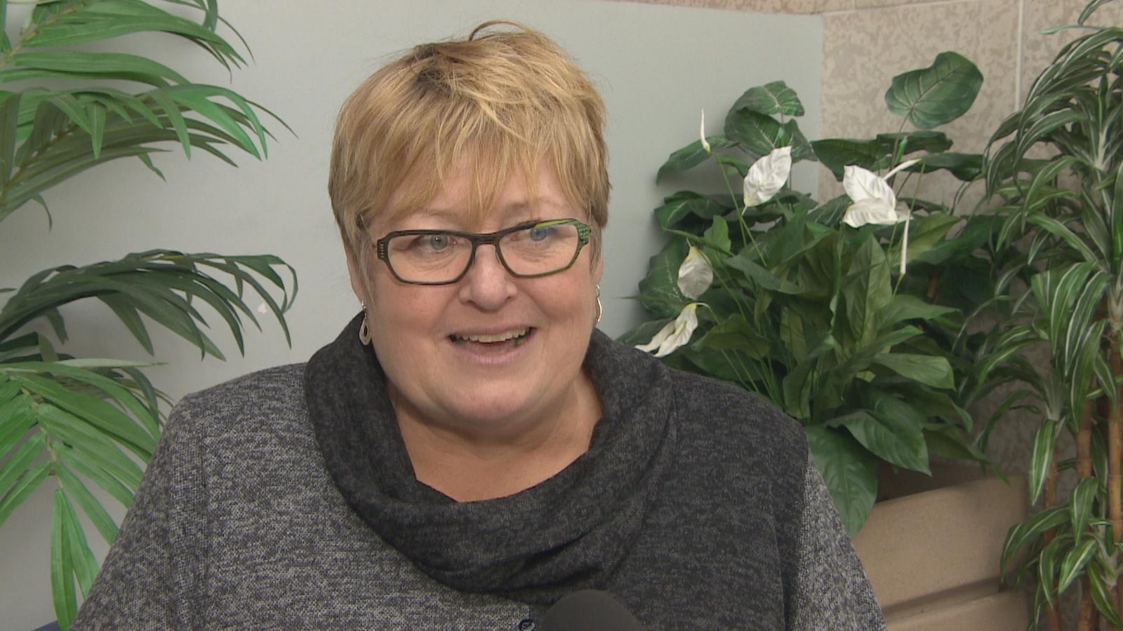 Marie-France Kenny accorde une entrevue devant un ensemble de plantes vertes.