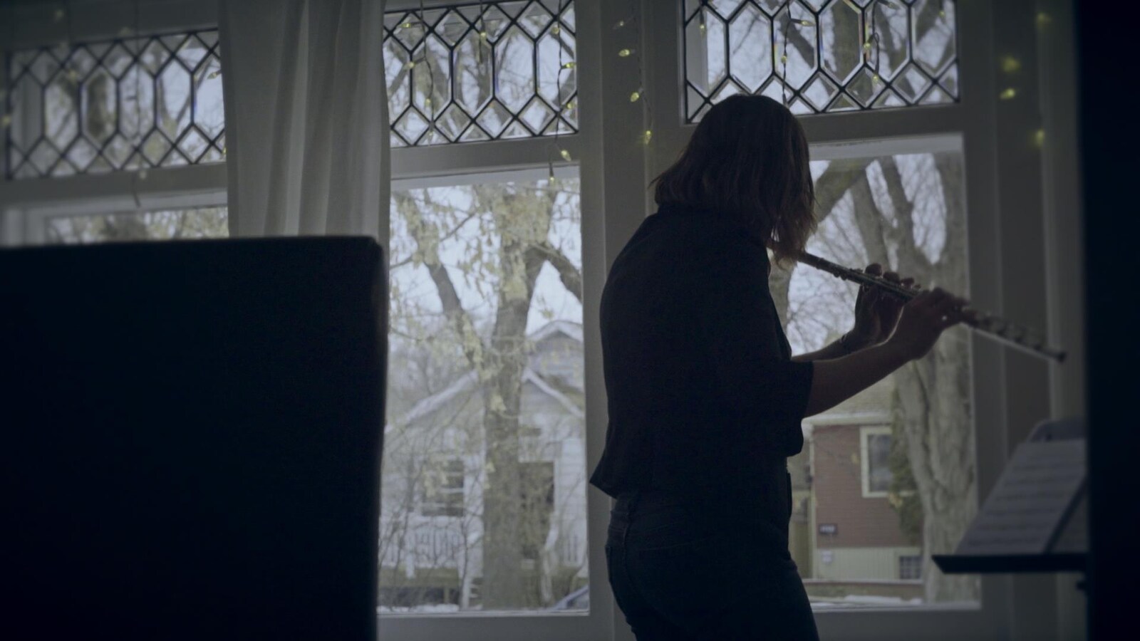 La musicienne Marie-Véronique Bourque joue de la flûte traversière de dos devant une fenêtre.