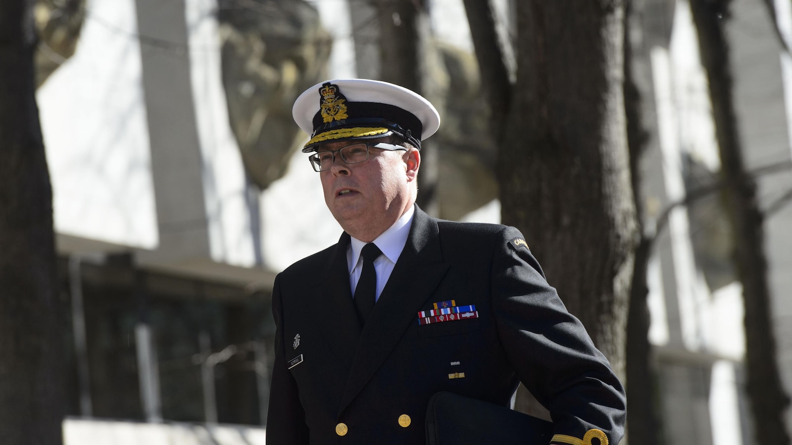 Un homme vêtu d'un veston couvert de grades et d'un chapeau de la marine royale canadienne marche à l'extérieur d'un palais de justice.