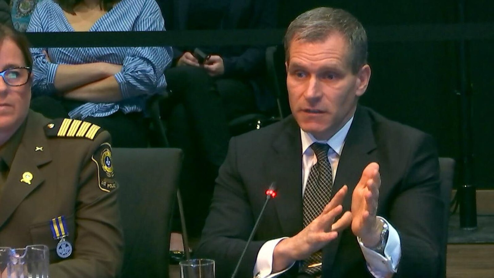 Martin Prud'homme, assis à une table, devant un micro, à côté d'une femme en uniforme.