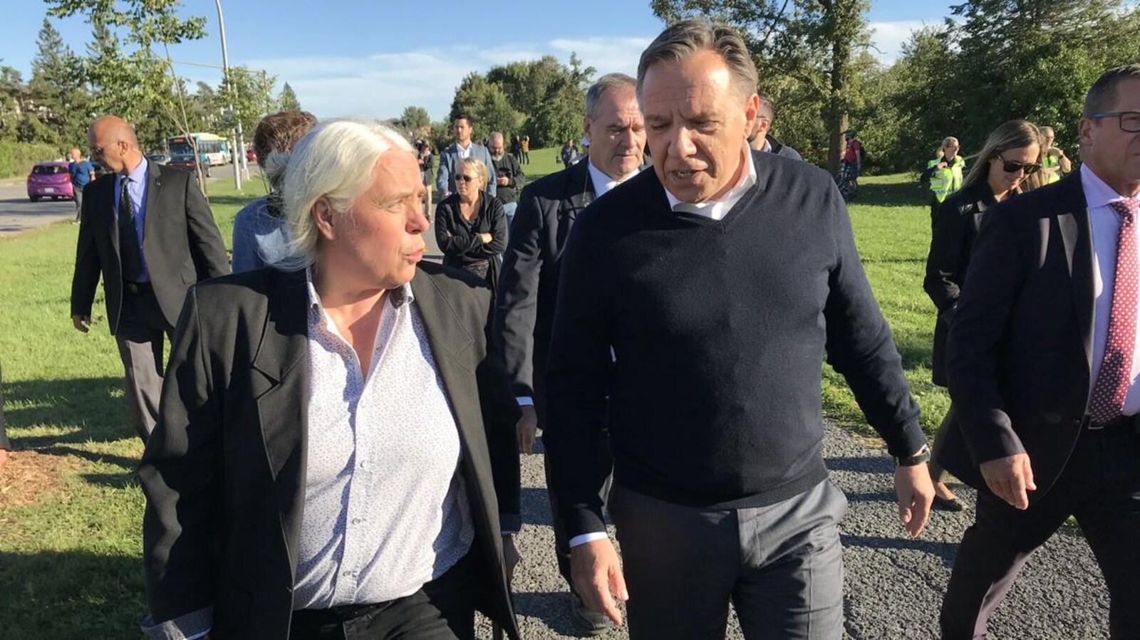 Manon Massé et François Legault discutent en marchant dans un parc de Gatineau près de bâtiments endommagés par la tornade.