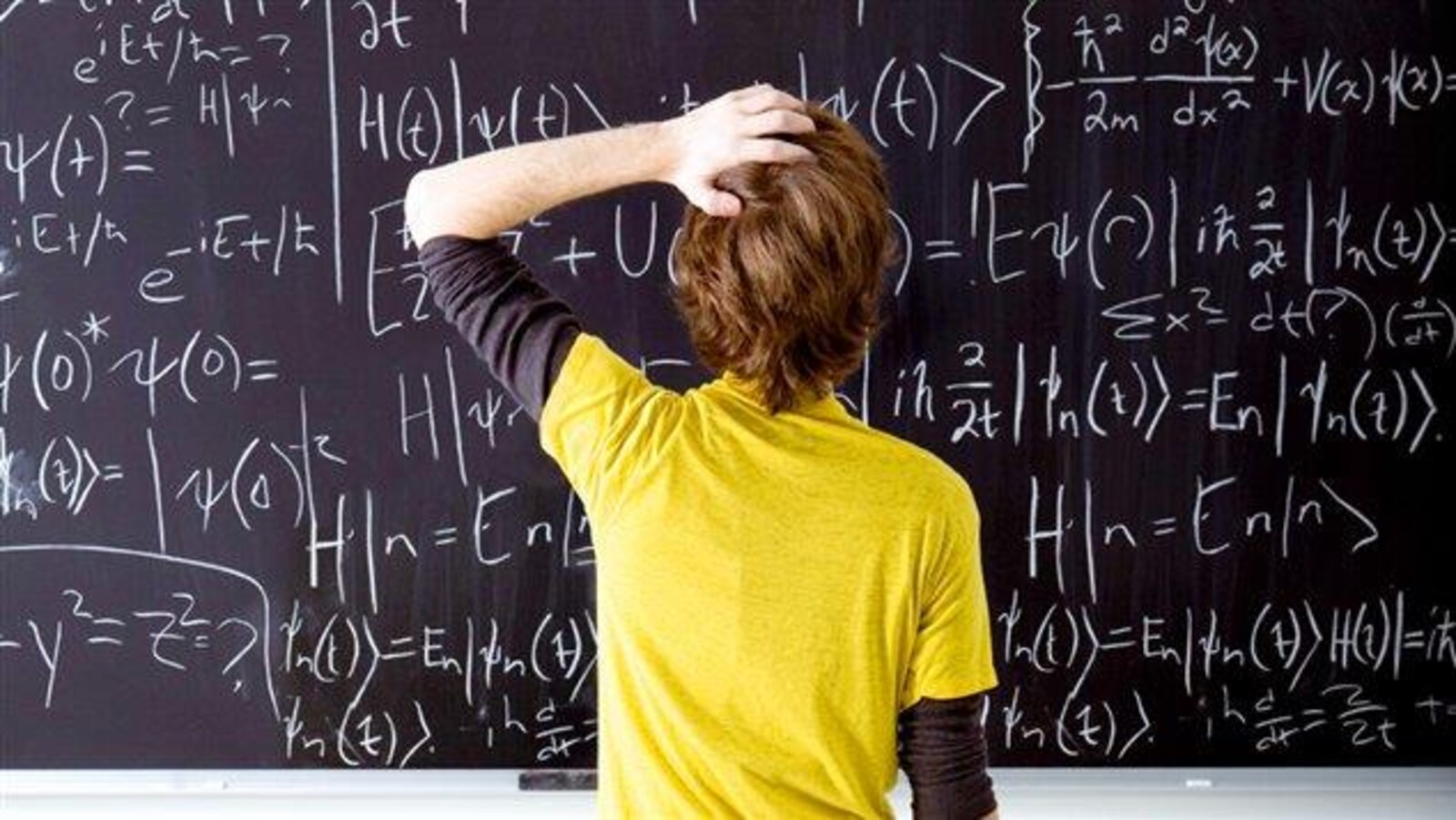 Un élève qui se gratte la tête devant un tableau rempli de formules mathématiques.