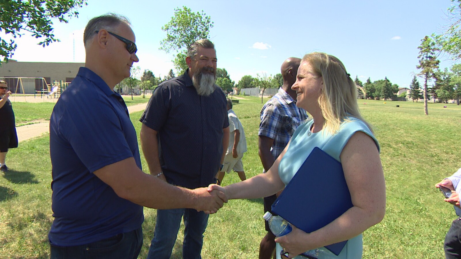 Le président de l'Association de la police de Winnipeg, Maurice Sabourin, serre la main de la candidate à la mairie, Jenny Motkaluk. Ils sont debout dehors sur un gazon.
