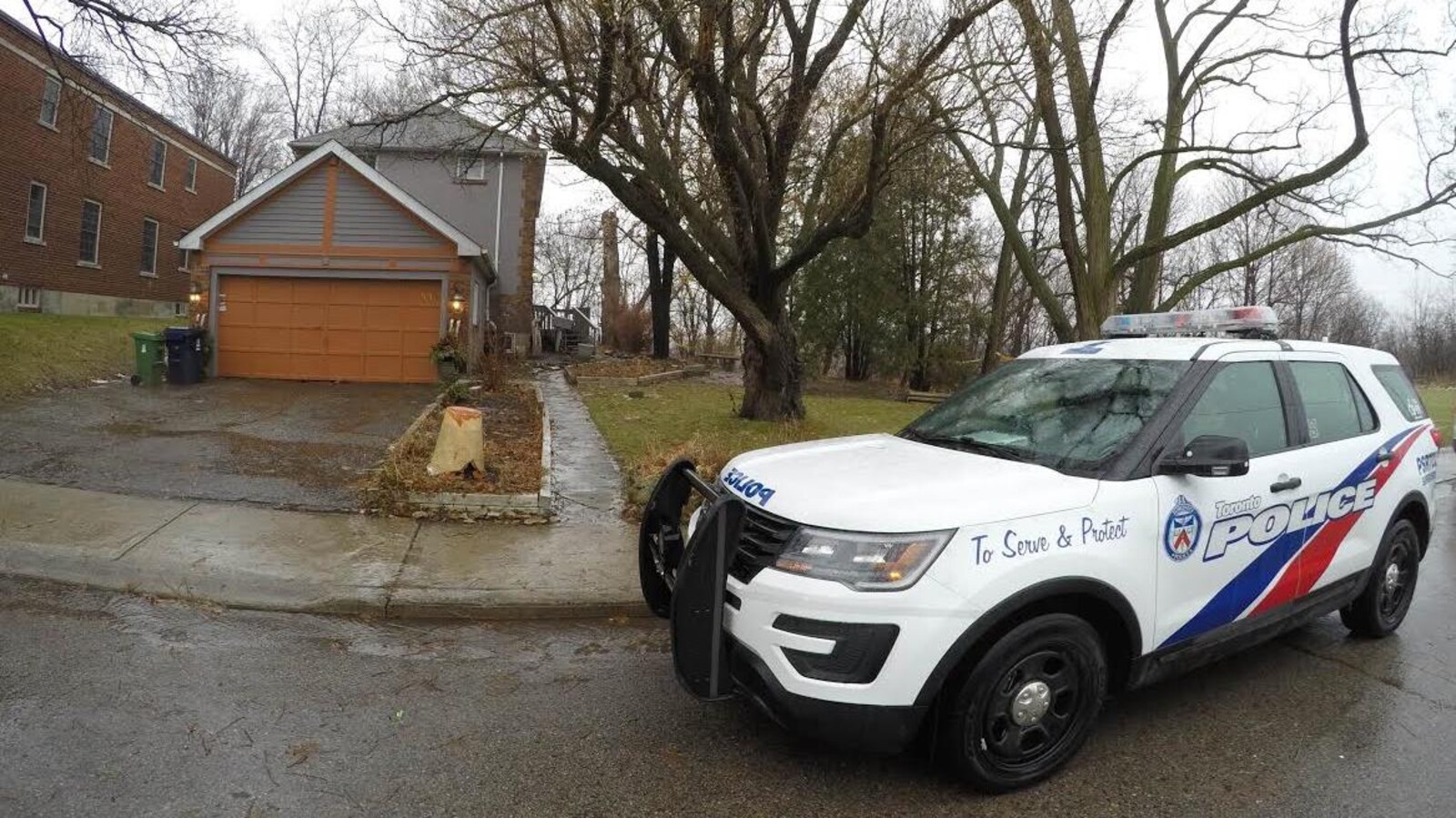 Photo d'un véhicule de police devant le garage d'une maison grise à deux étages.