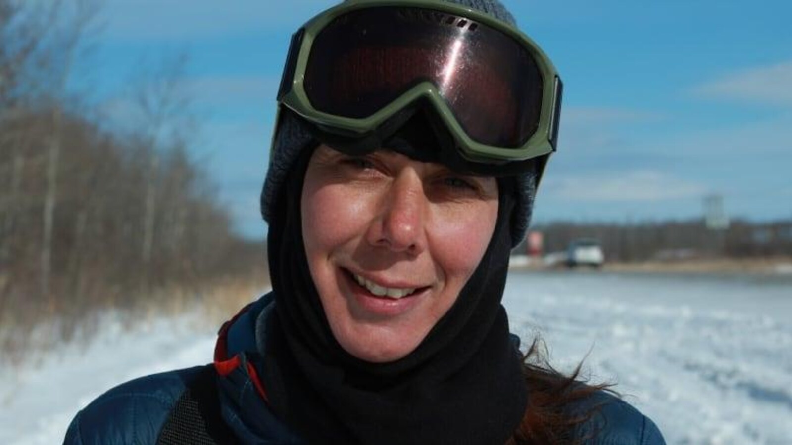 Gros plan sur le visage souriant de Melanie Vogel, vêtue pour l'hiver avec ses lunettes de ski relevées sur son front.