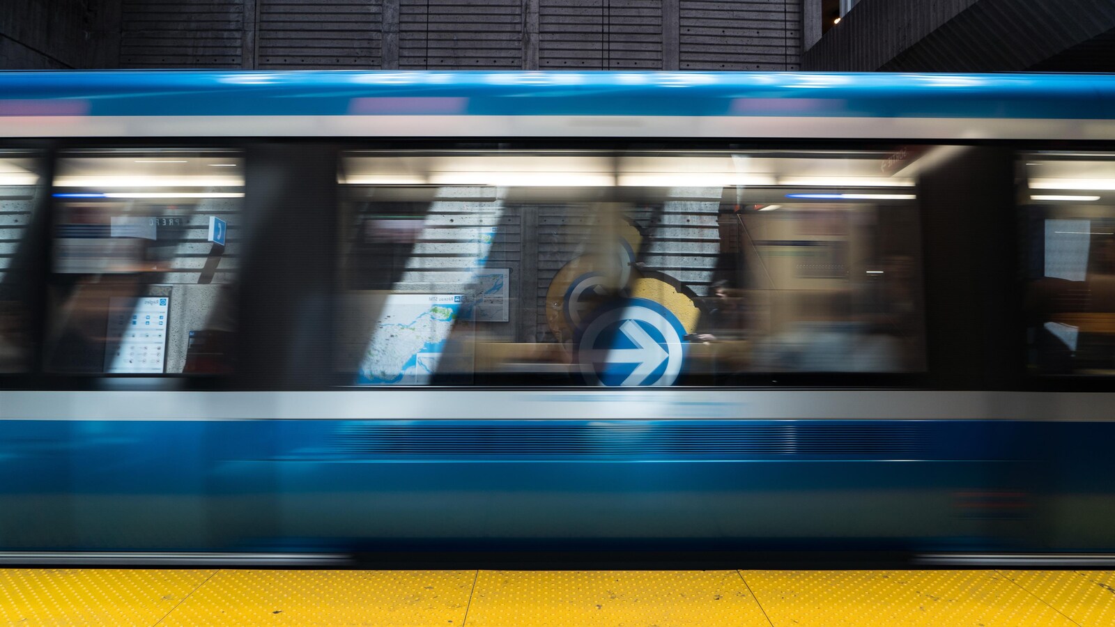 Un train du métro de Montréal passe rapidement au quai d'une station.