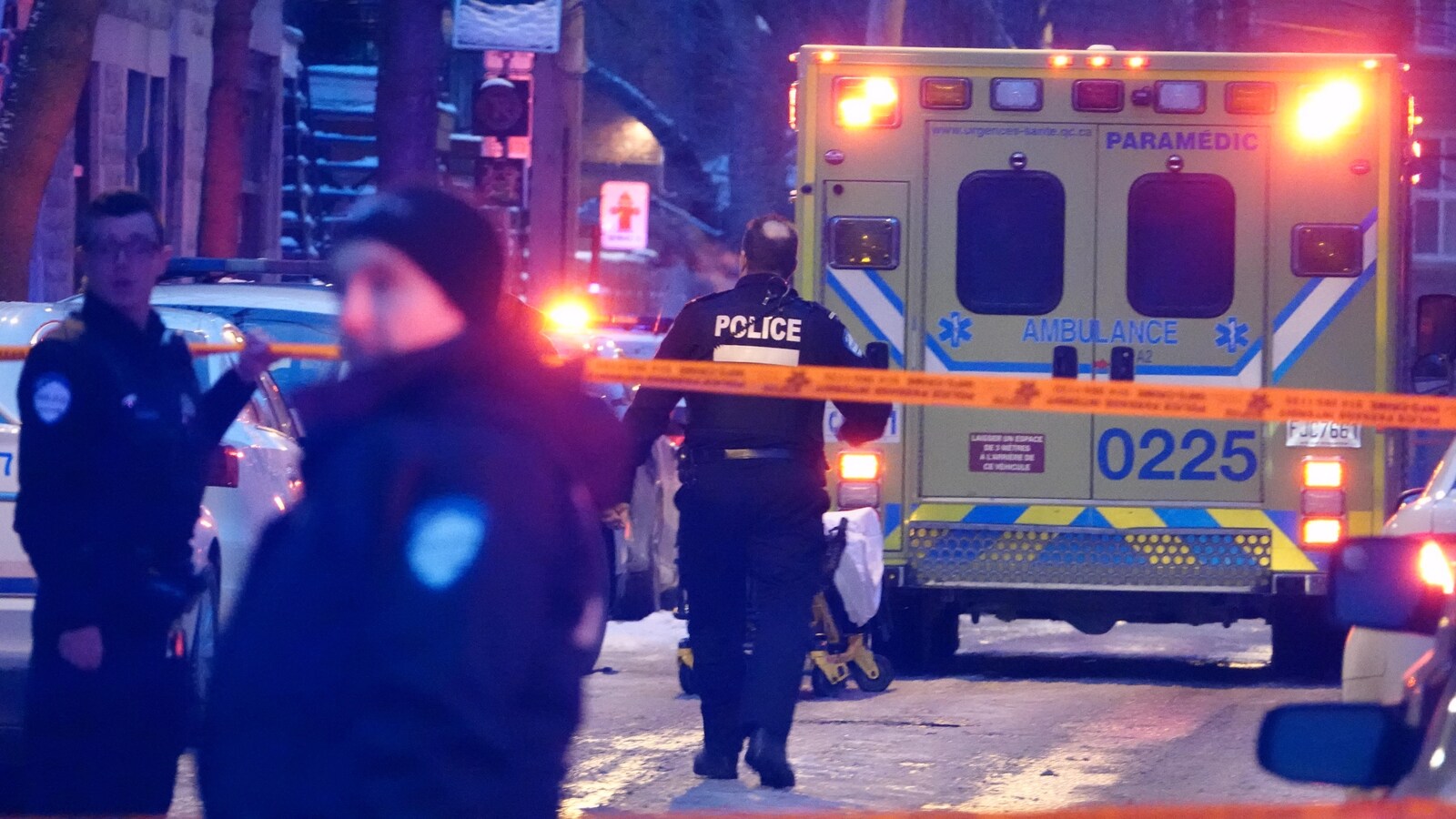 Un policier, vu de dos, marche dans la rue vers une ambulance.