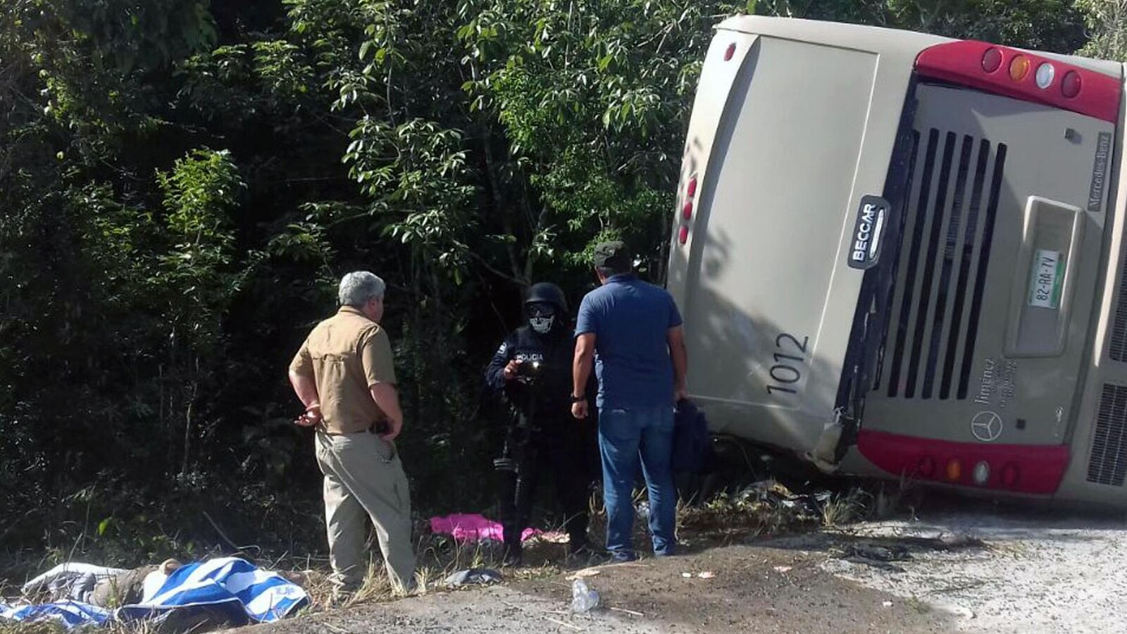 Des policiers mexicains et des ambulanciers près d'un autocar renversé sur le côté d'une route mexicaine.