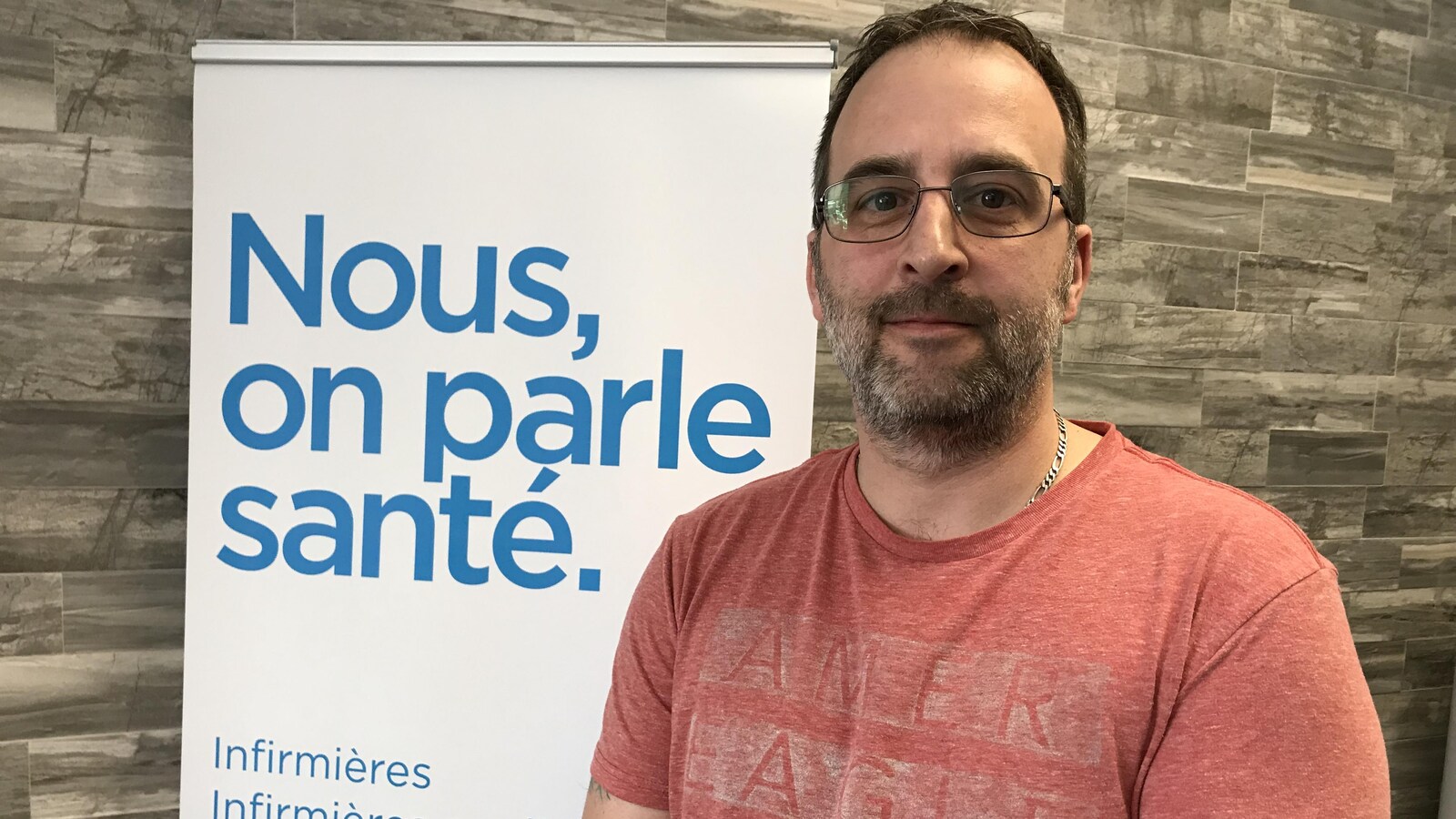 Un homme sourit à la caméra devant une affiche indiquant «Nous, on parle santé».