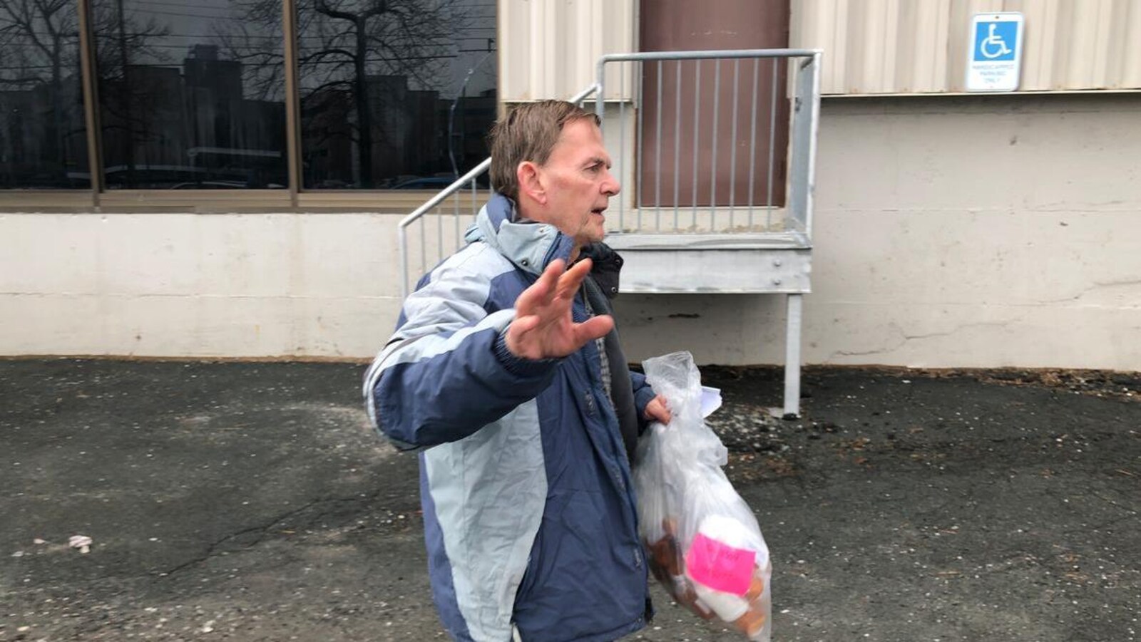 L'accusé, Michael Patrick McNutt, marche devant le palais de justice de Dartmouth en faisant un geste de la main pour éloigner les micros et caméras.