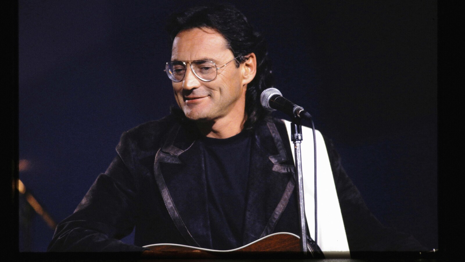 Le musicien est sur scène et sourit devant un micro.