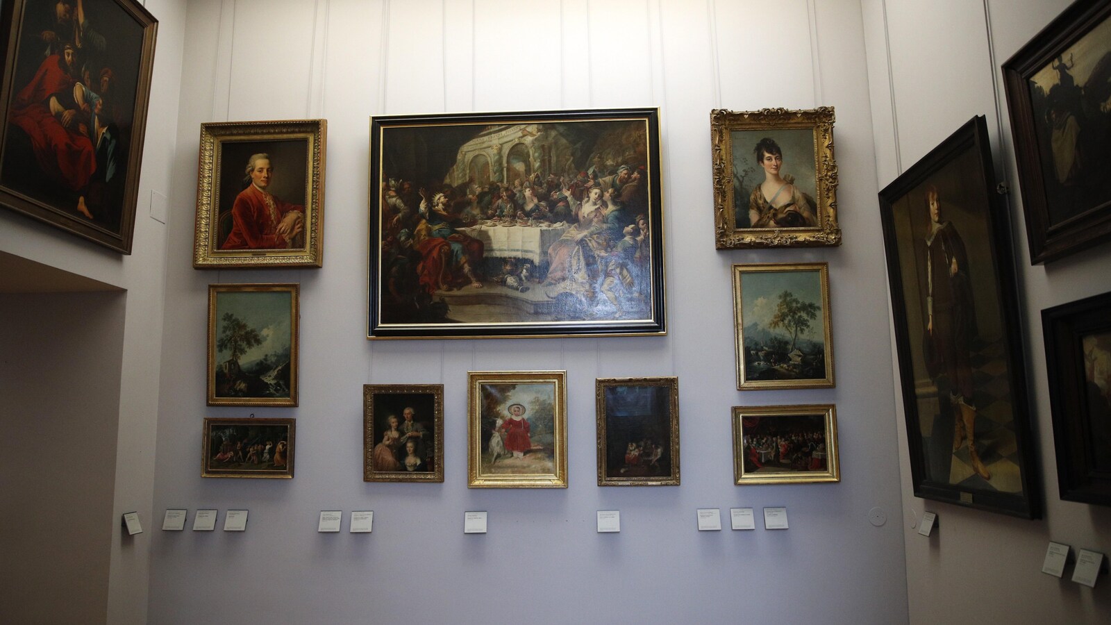 Plusieurs peintures de diverses tailles sont accrochées aux murs d'une salle du Louvre