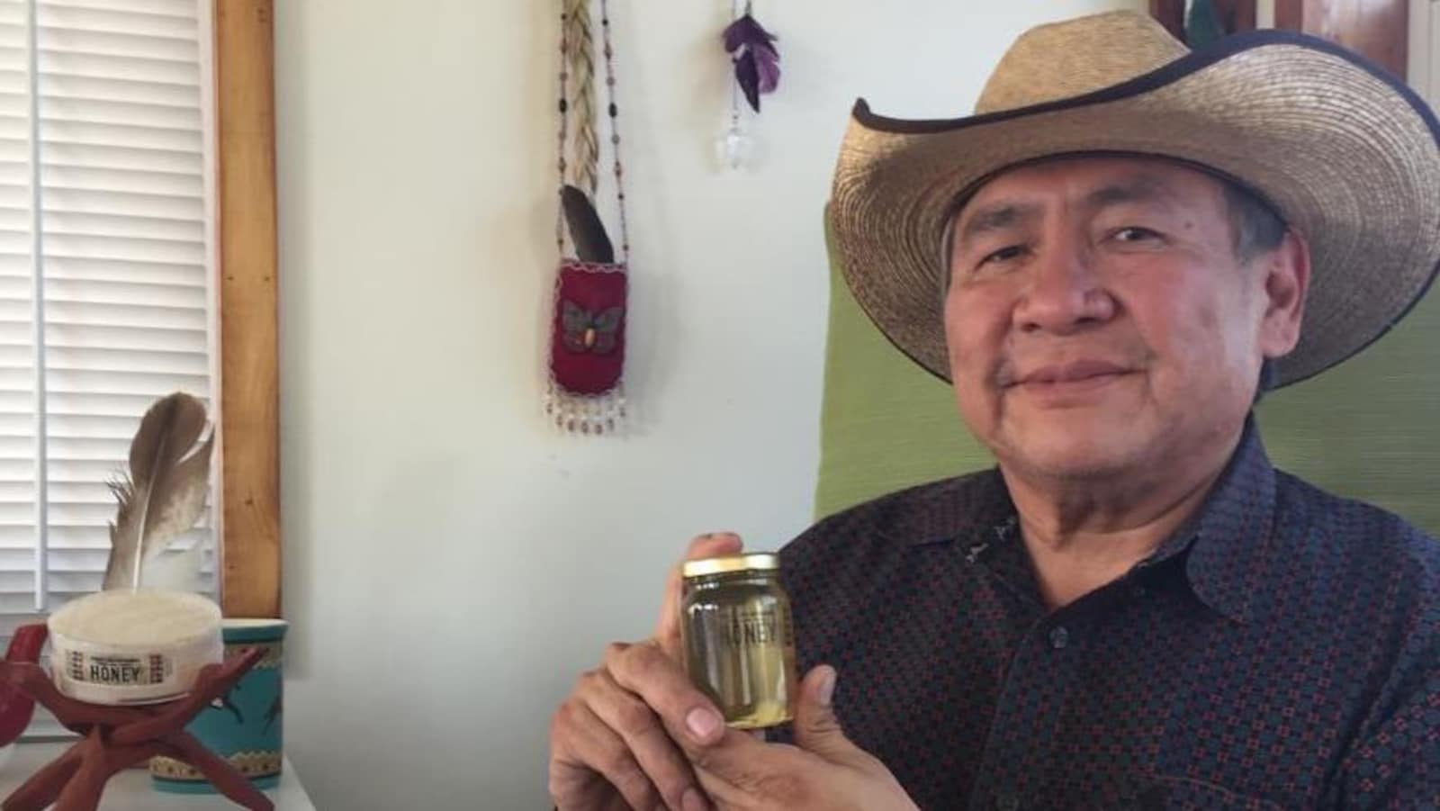 Lee Crowchild tient fièrement une bouteille de miel devant lui.