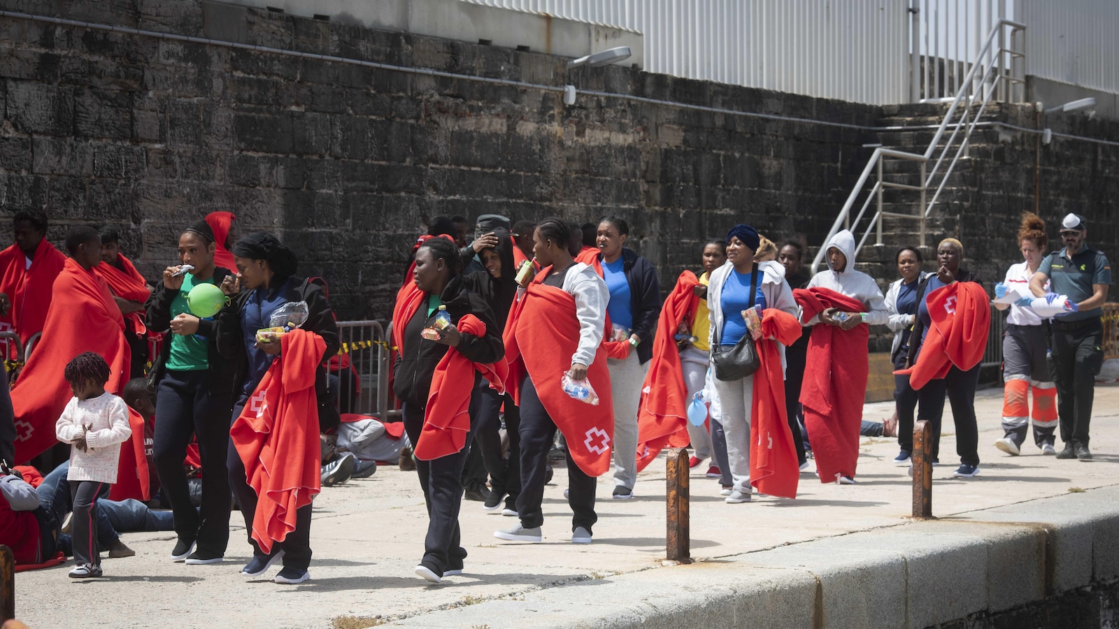 Des dizaines de migrants marchent le long d'un quai dans le port de Tarifa avec des couvertures fournies par la Croix rouge espagnole.