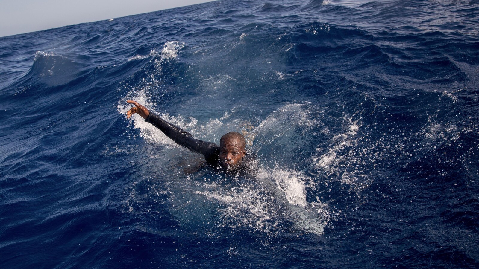 Un migrant, la tête sortie de l'eau, semble nager.