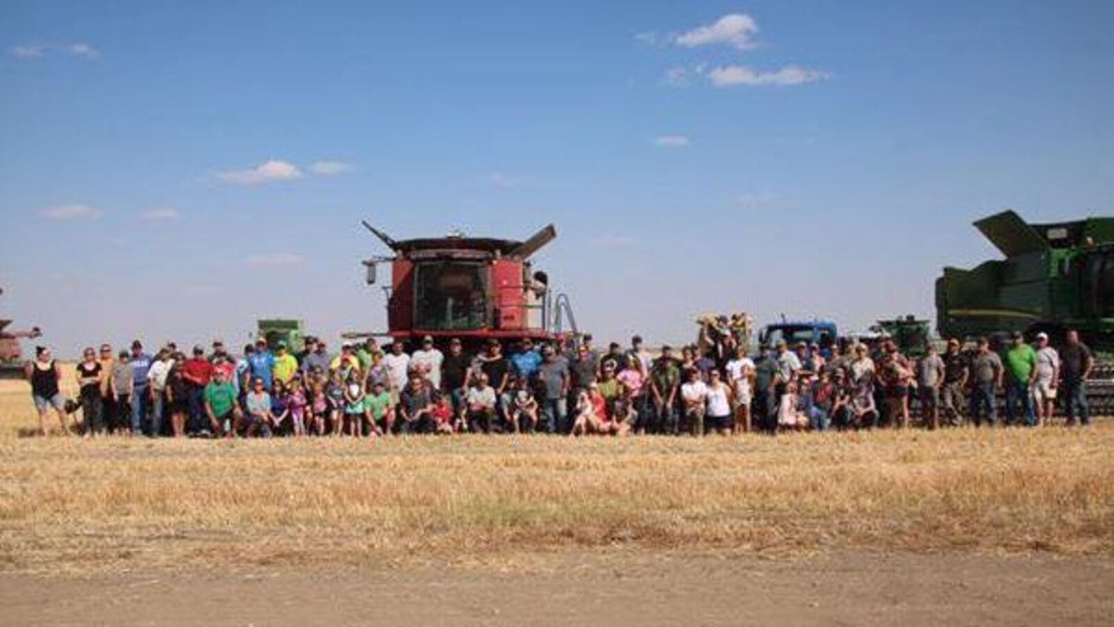 Un grand groupe pose dans un champ devant des moissonneuses-batteuses.