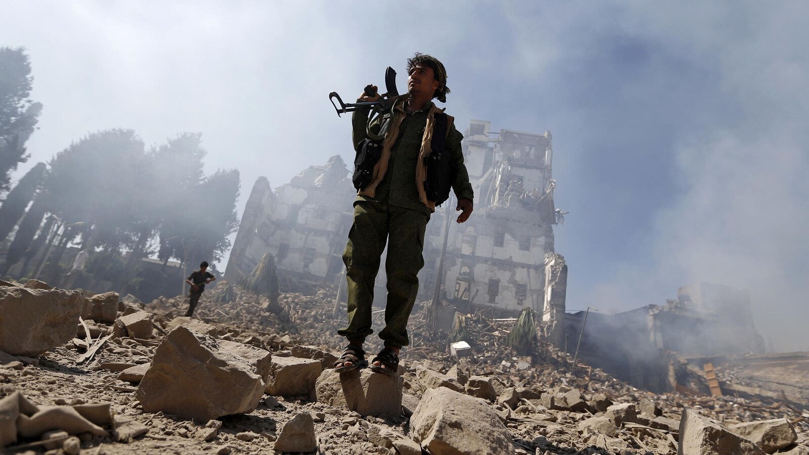 Un milicien houthi armé se tient debout devant un immeuble détruit.