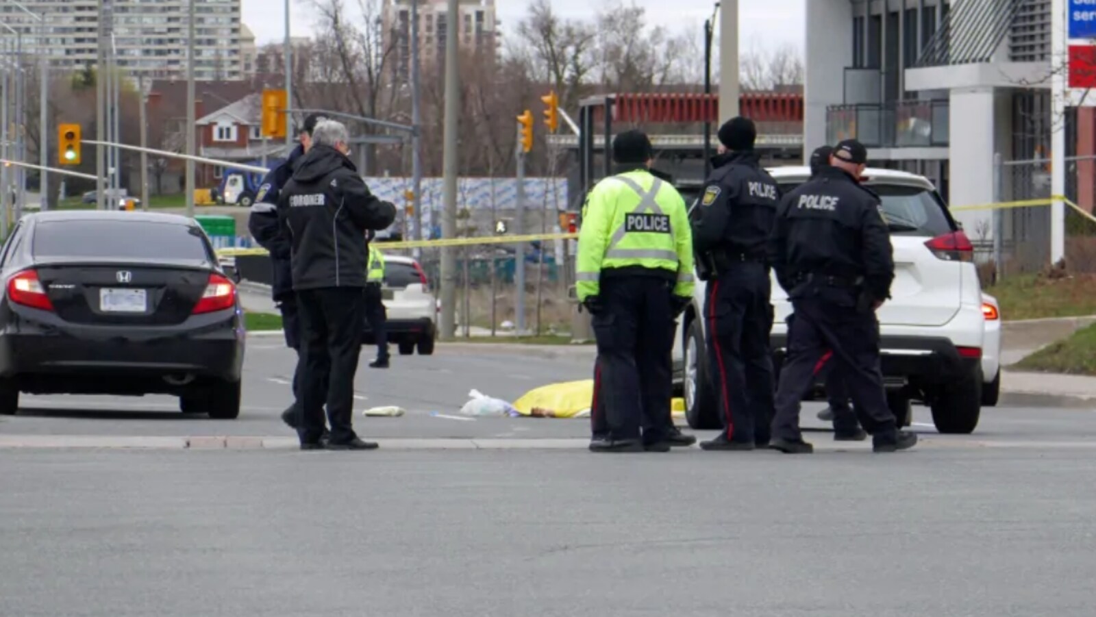 Photo de policiers se tenant debout dans une rue près de véhicules et d'une banderole de police jaune.
