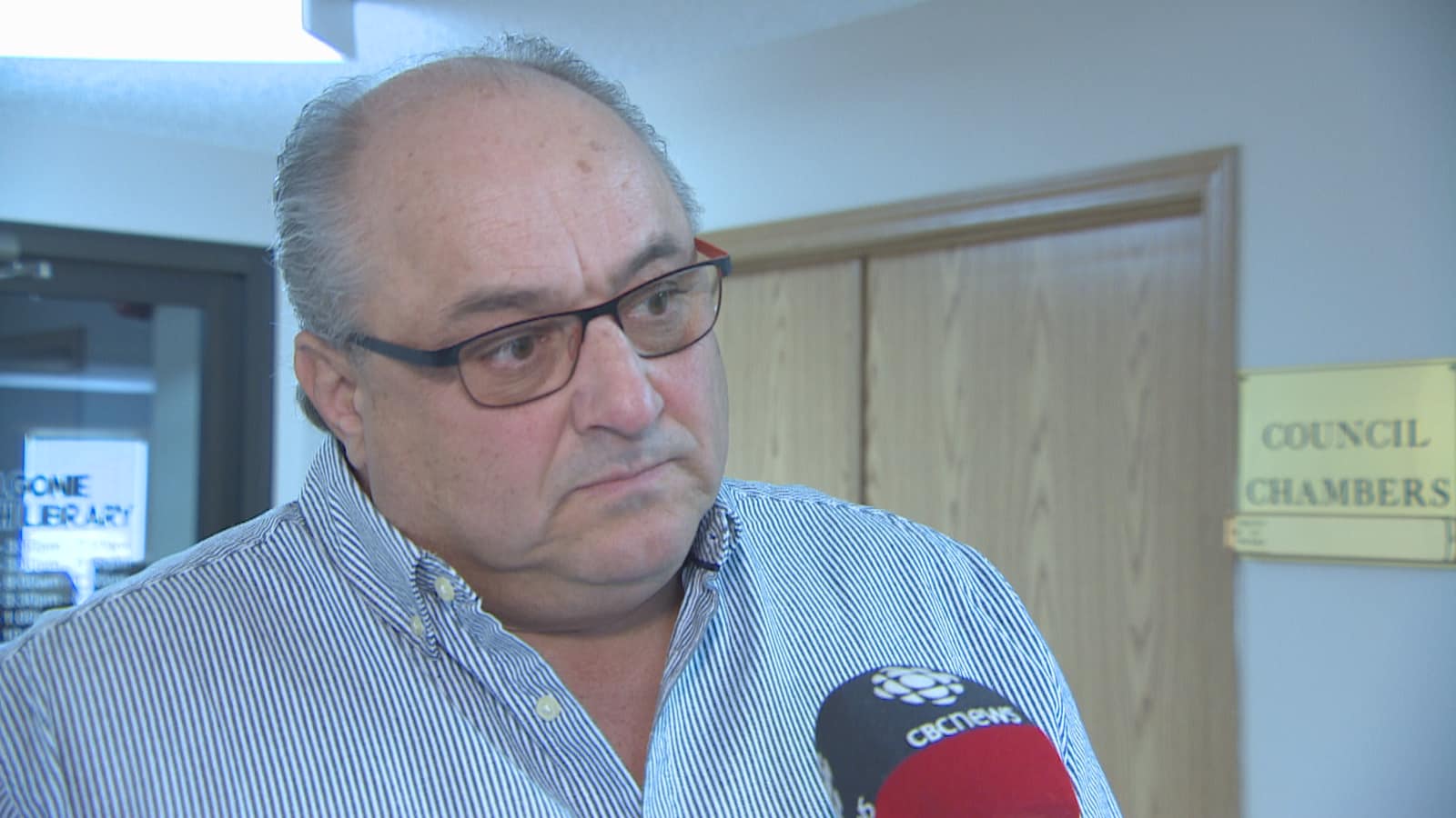 Plan serré de Mitchell Huber devant la salle de réunion du conseil municipal.