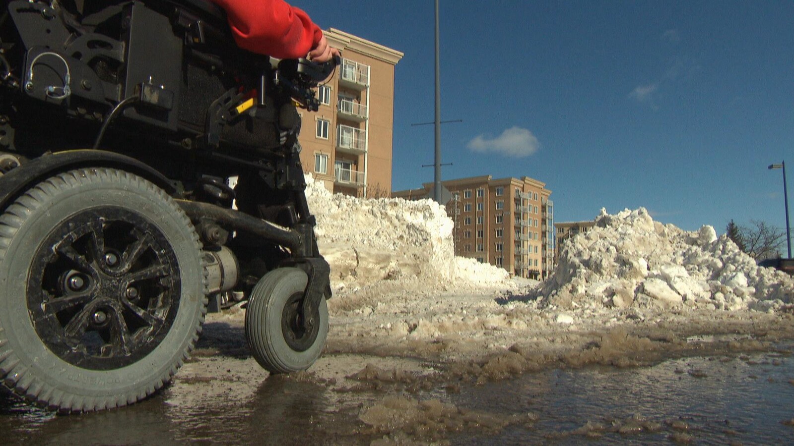 Une personne en fauteuil roulant électrique circule sur un trottoir inondé.