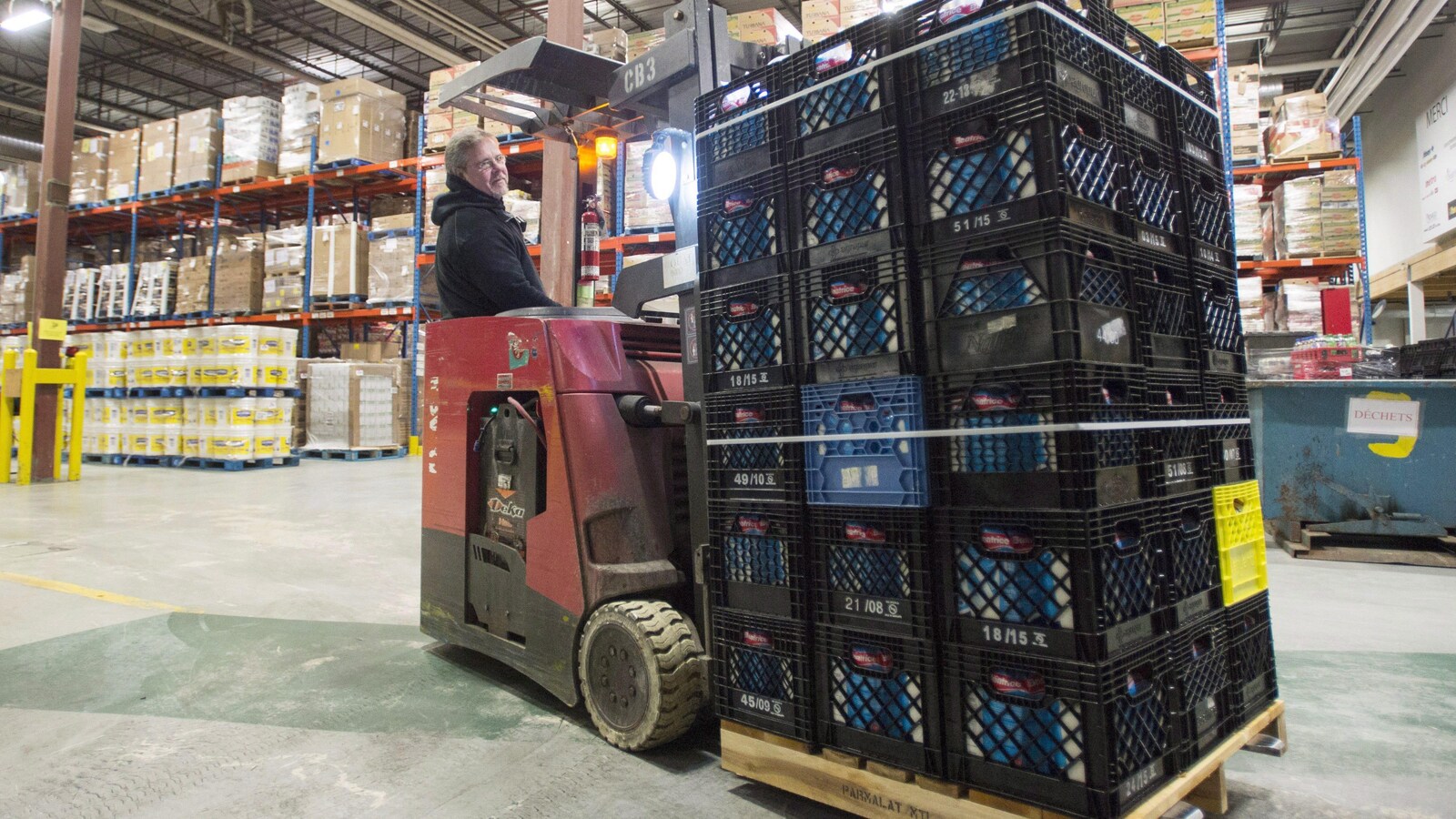 Un bénévole manoeuvre un engin de manutention transportant des caisses de lait dans un entrepôt de l'organisme Moisson Montréal.