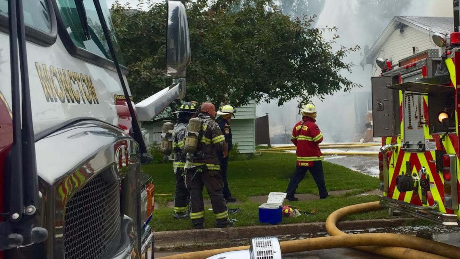 Un groupe de pompiers devant une maison qui dégage de la fumée