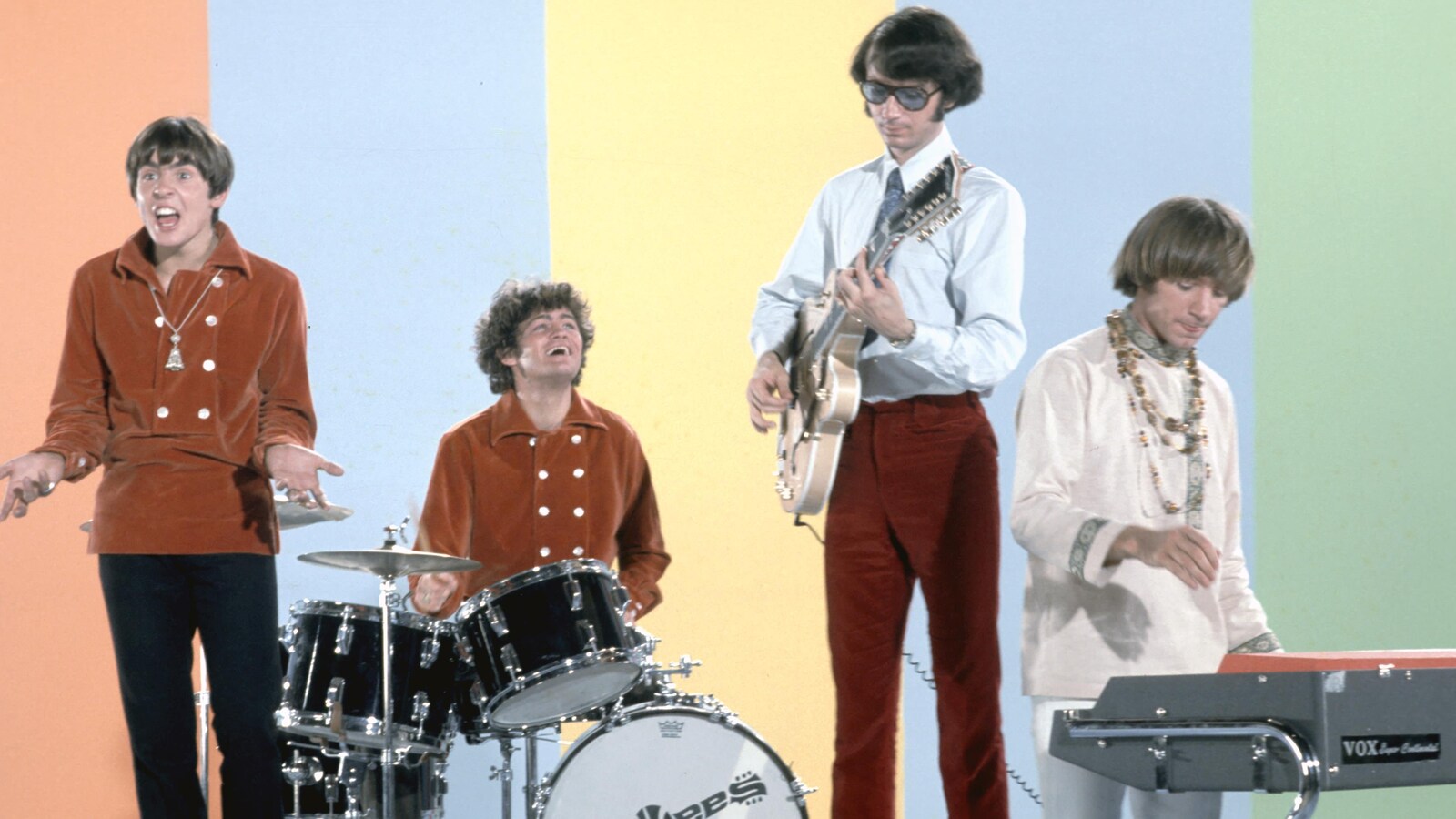 Les quatre musiciens jouent devant un fond coloré.