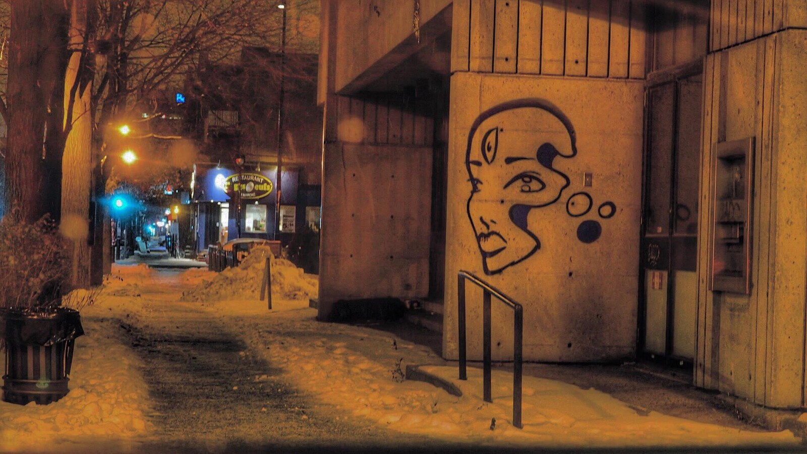 Une rue déserte est enneigée tôt le matin à Montréal. On voit un graffiti sur un mur.