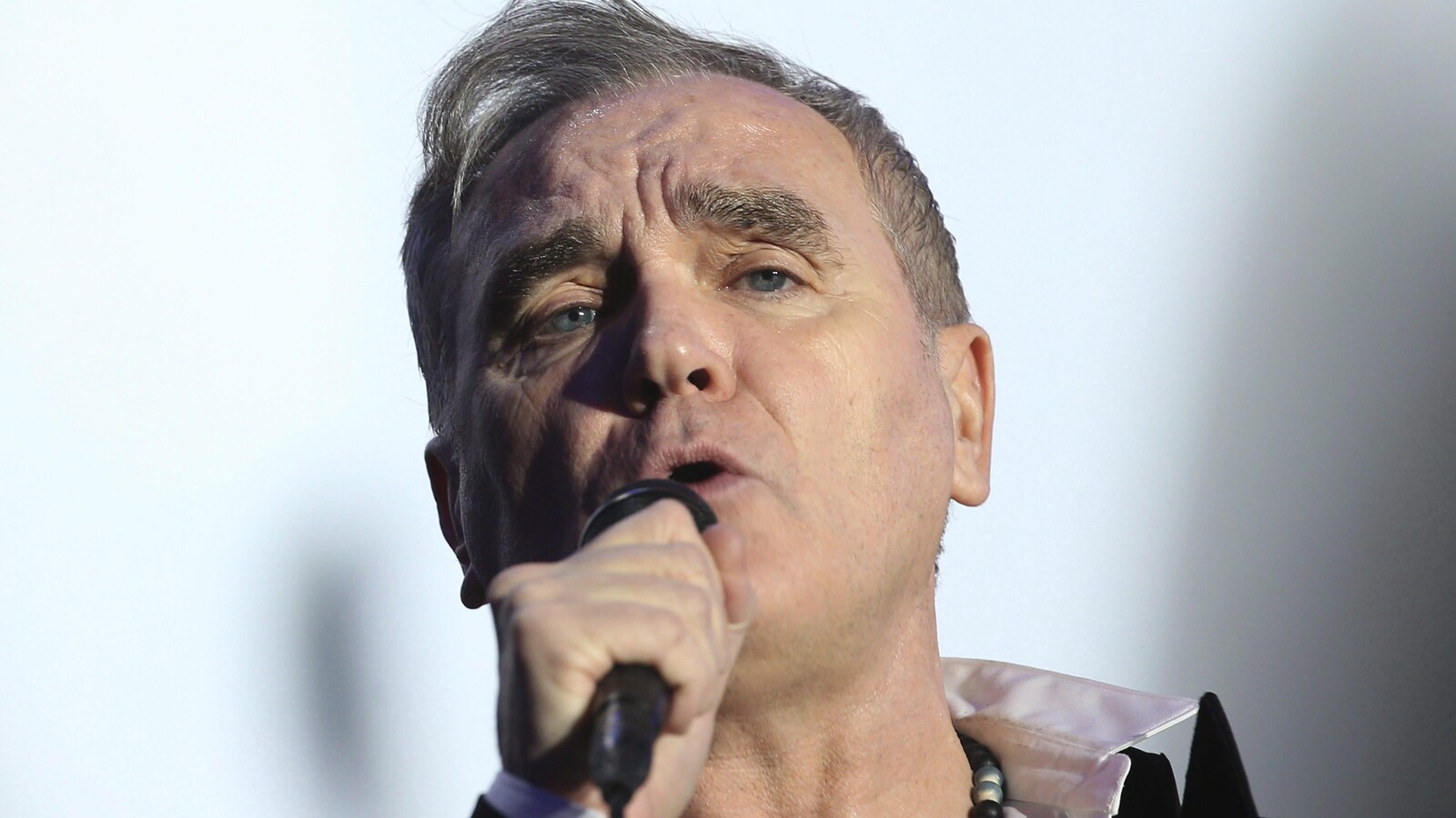 Le chanteur Morrissey en concert tient son micro à la main en faisant face à l'appareil photo.