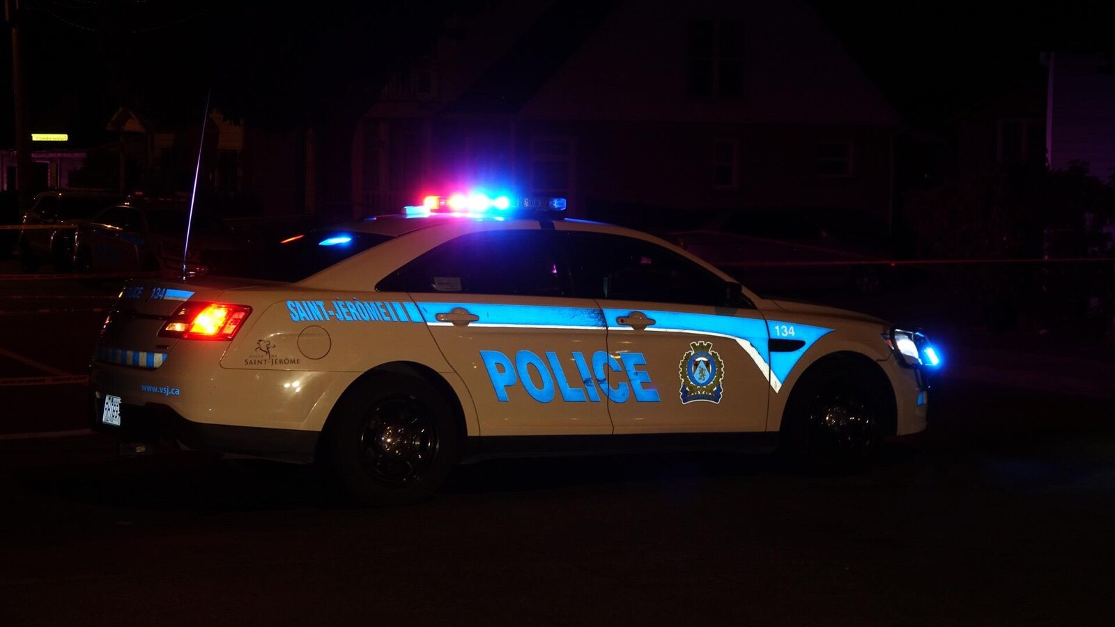 Une voiture du Service de police de Saint-Jérôme, dans les Laurentides, est stationnée de nuit sur une route avec les gyrophares allumés.